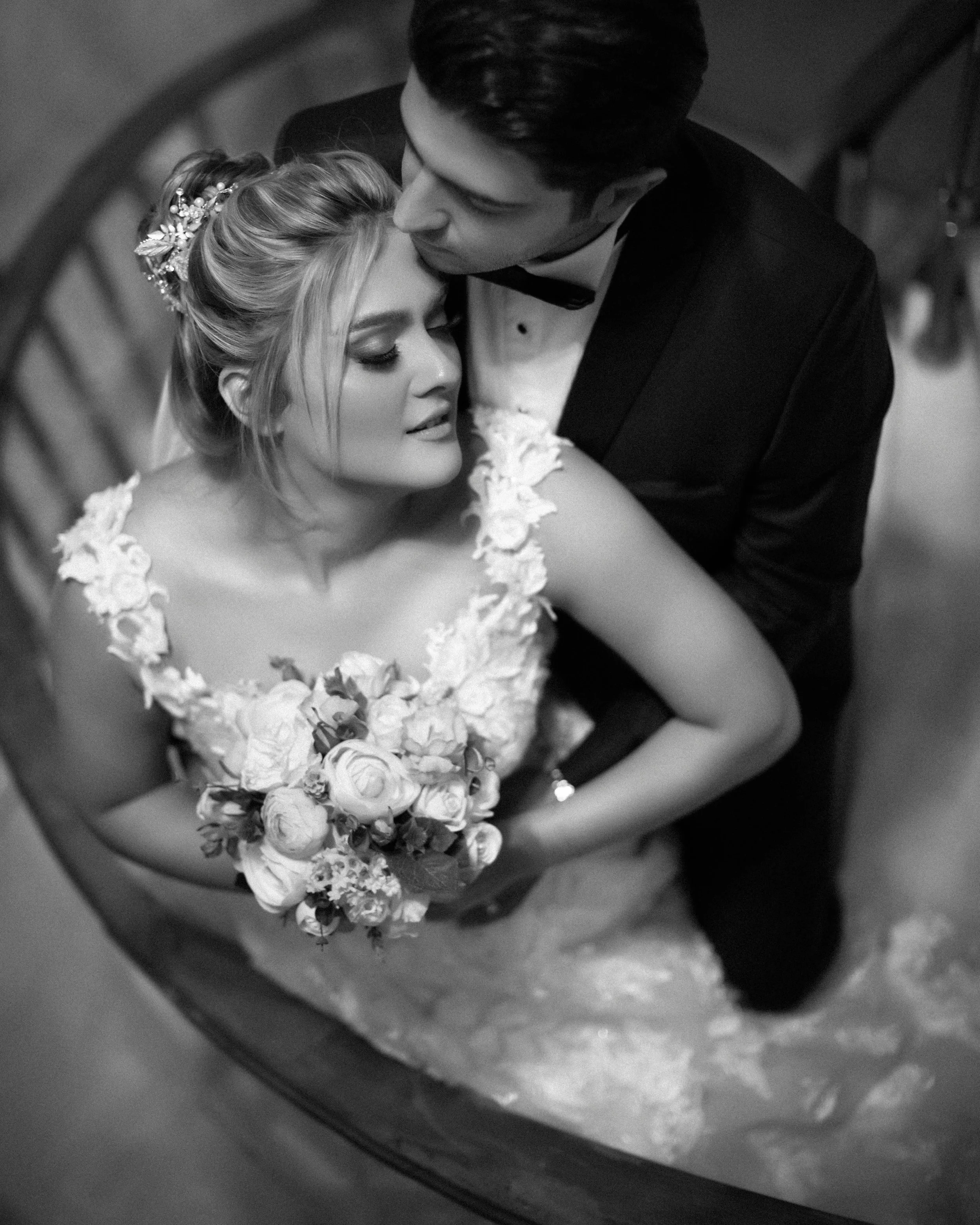 Black and white photo of a bride and groom close together, with the bride holding a bouquet of flowers, sitting in a boat.