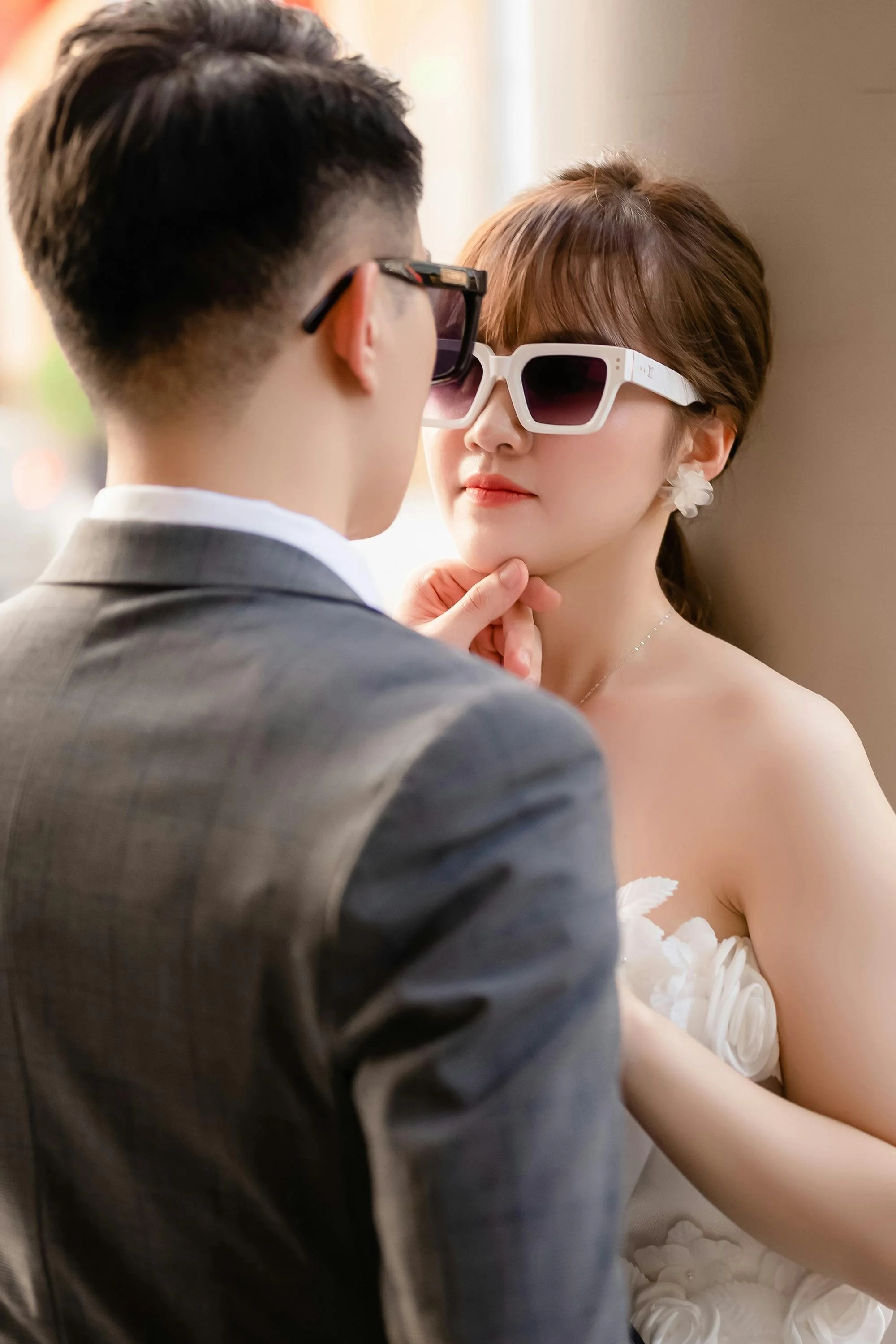 A man and woman wearing sunglasses share an intimate moment, with the man touching the woman's chin as they look at each other.