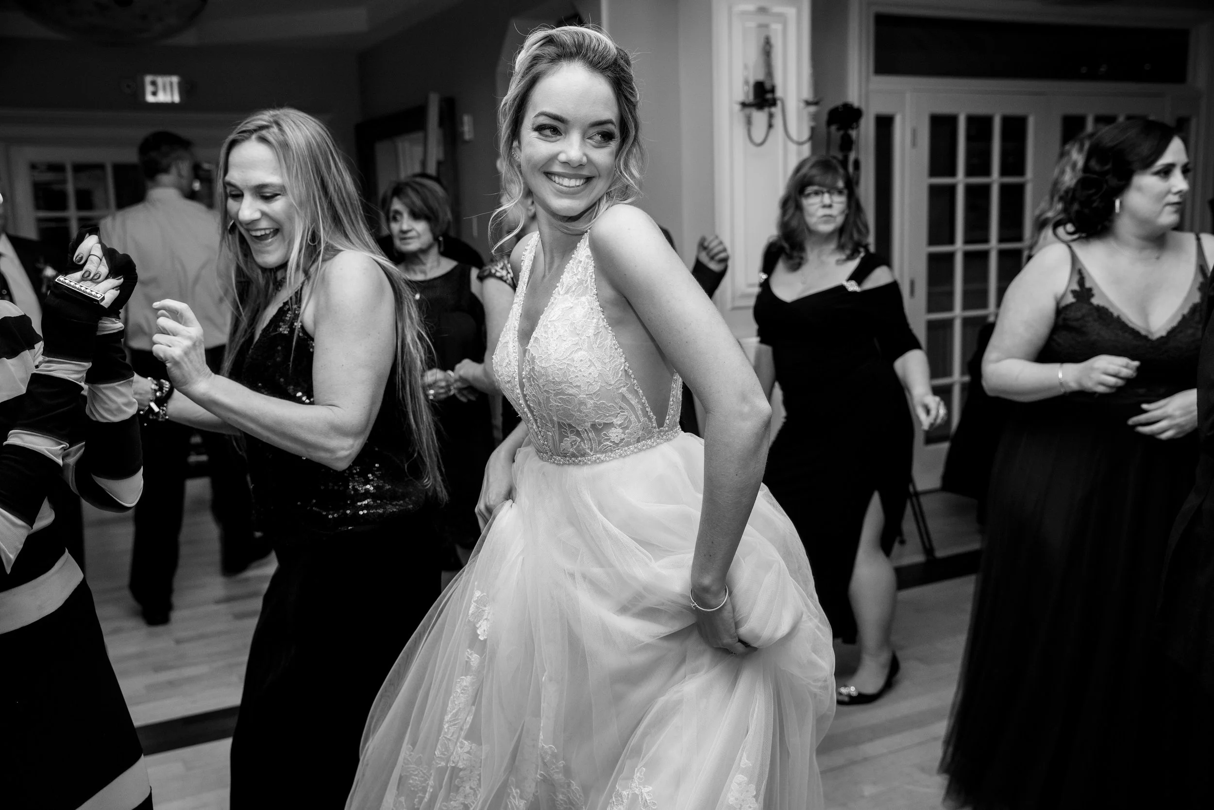 A bride in a wedding dress dancing at a wedding reception with several women and guests dancing in the background.