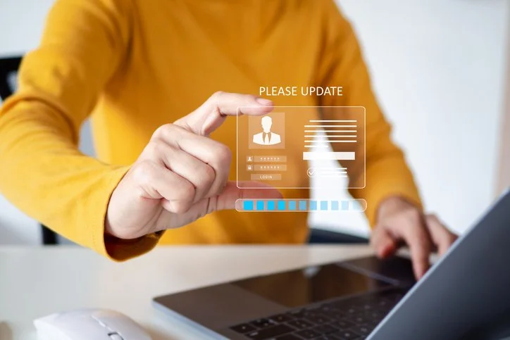 Person in a yellow shirt interacting with a virtual login screen over a laptop, with the screen displaying profile and password prompts.