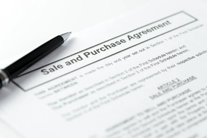 Close-up of a sale and purchase agreement document with a black pen resting on it.
