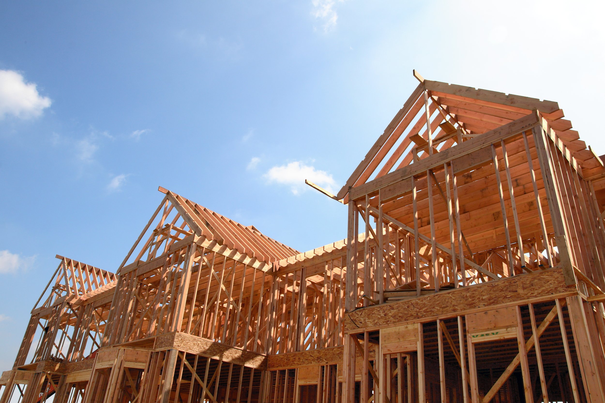 Wooden framework of a house under construction against a blue sky with some clouds.