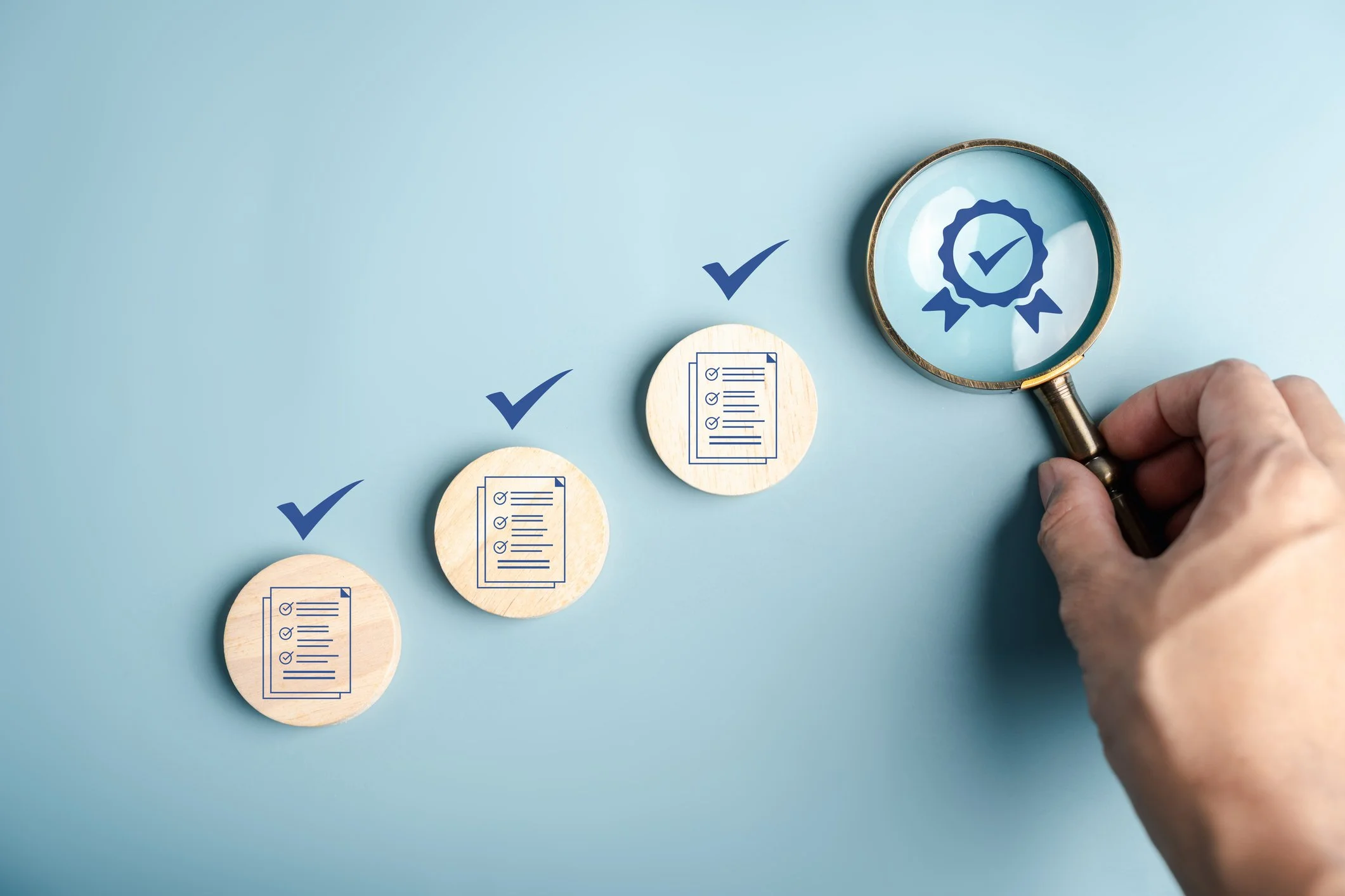 Hand holding a magnifying glass over a checklist with checkmarks, symbolizing review and quality assurance.