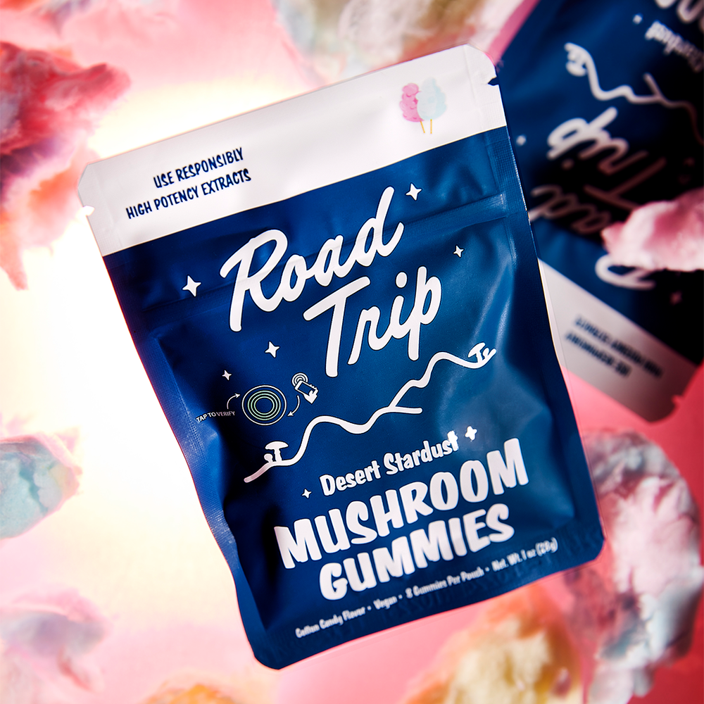 A blue and white bag of Road Trip Mushroom Gummies with desert stardust flavor, surrounded by cotton candy in the background.