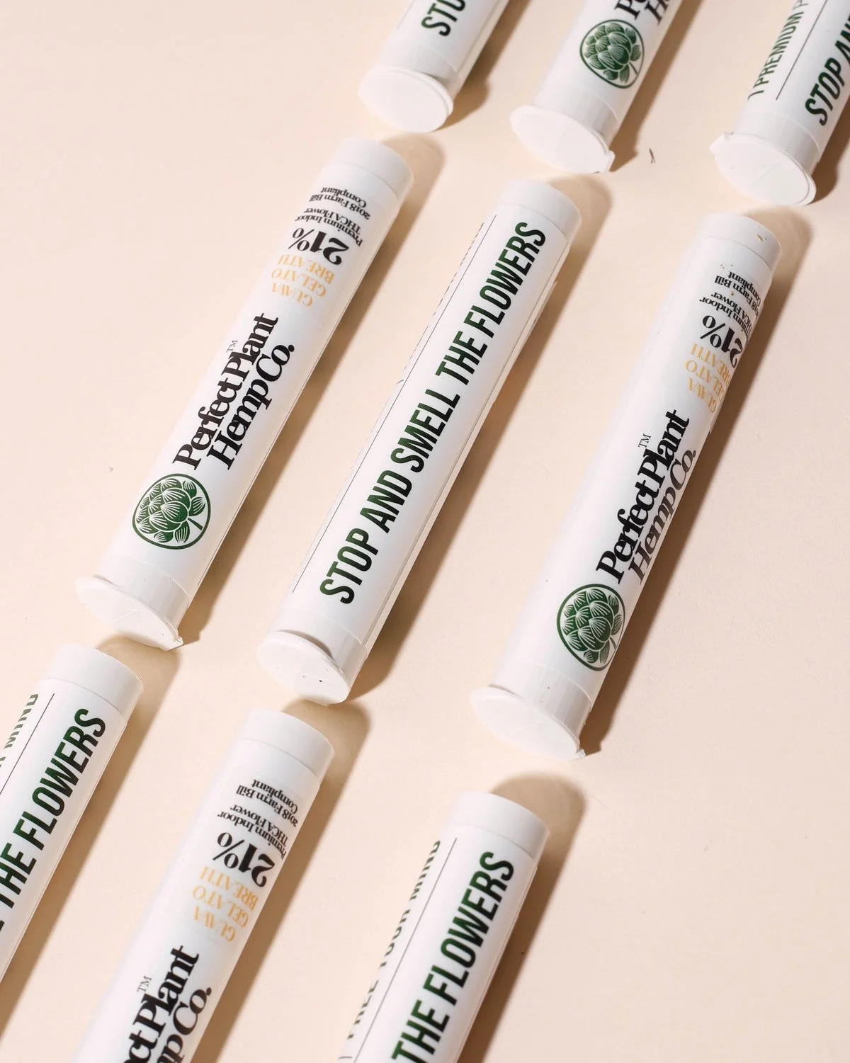 Multiple lip balm tubes with the label 'Perfect Plant Hemp Co.' and one tube with a message in green text saying 'STOP AND SMELL THE FLOWERS' on a beige background.