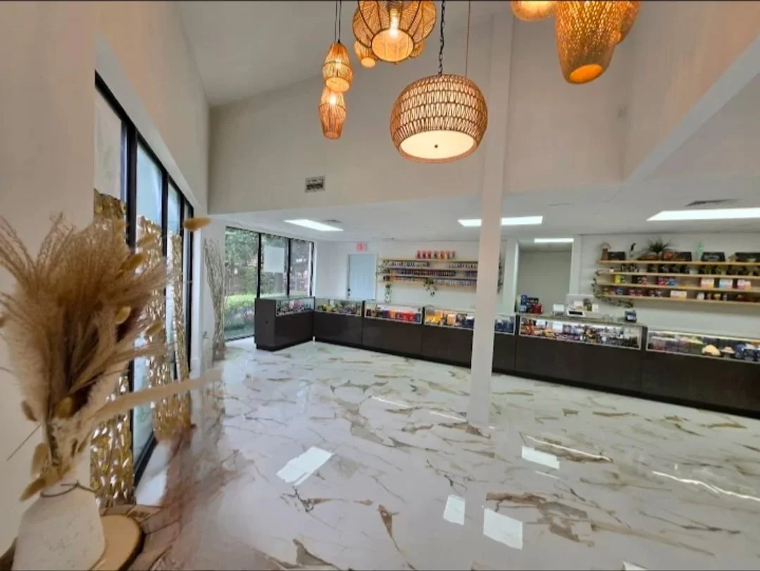 Interior of a modern store with large windows, decorative hanging lamps, a white marble floor, and shelves filled with various items.
