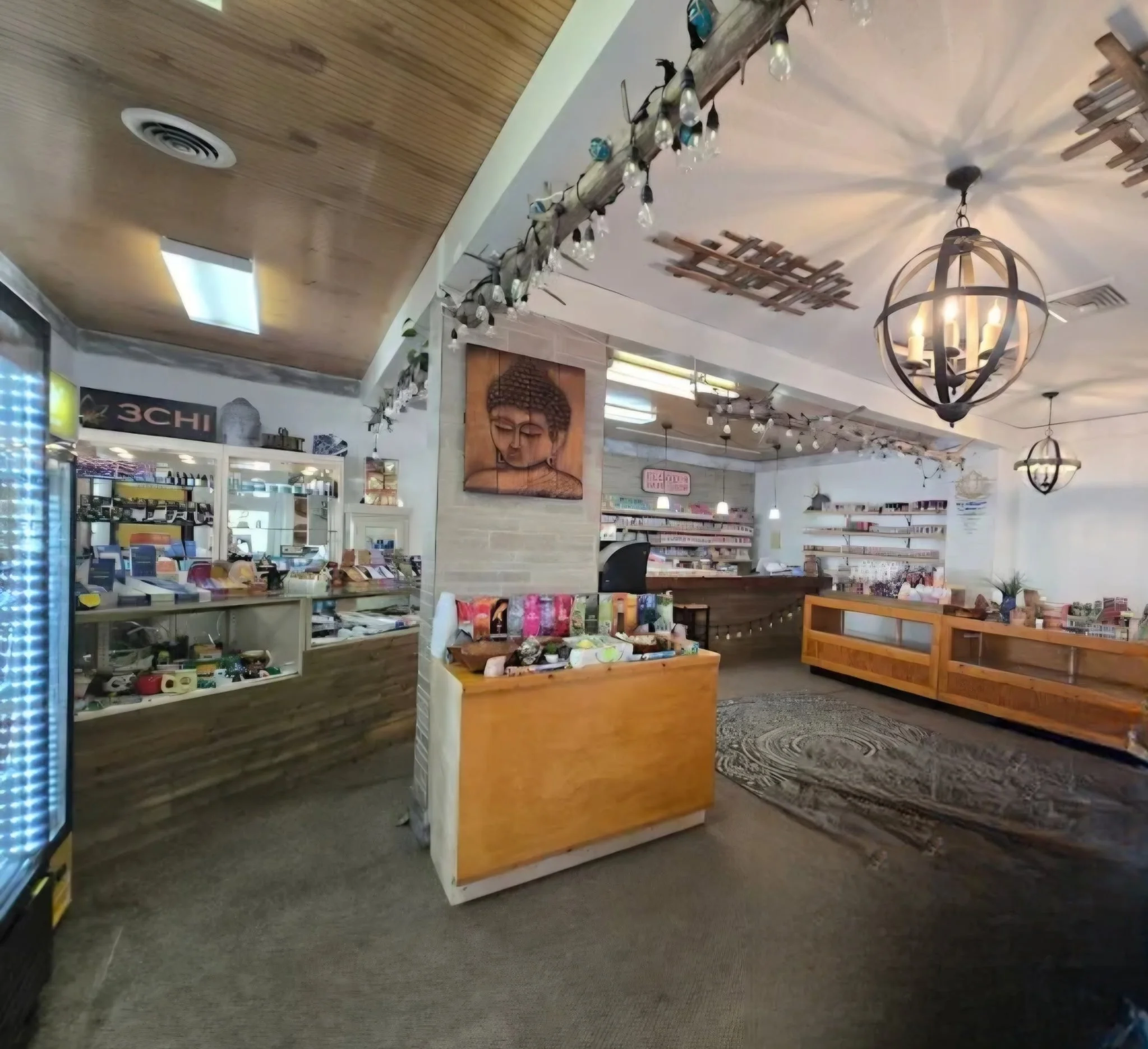 Interior of a store with wooden fixtures, a Buddha wall art, hanging light fixtures, and shelves with various products.