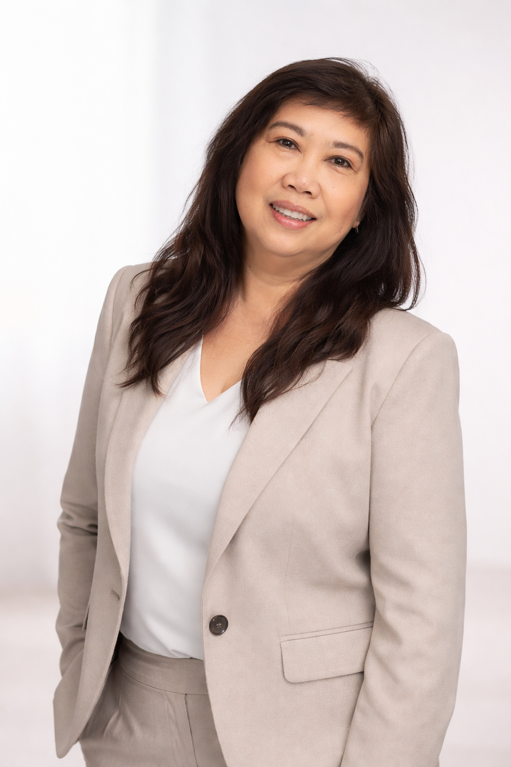 Professional woman with dark brown hair in a beige suit and white blouse, smiling against a plain white background.