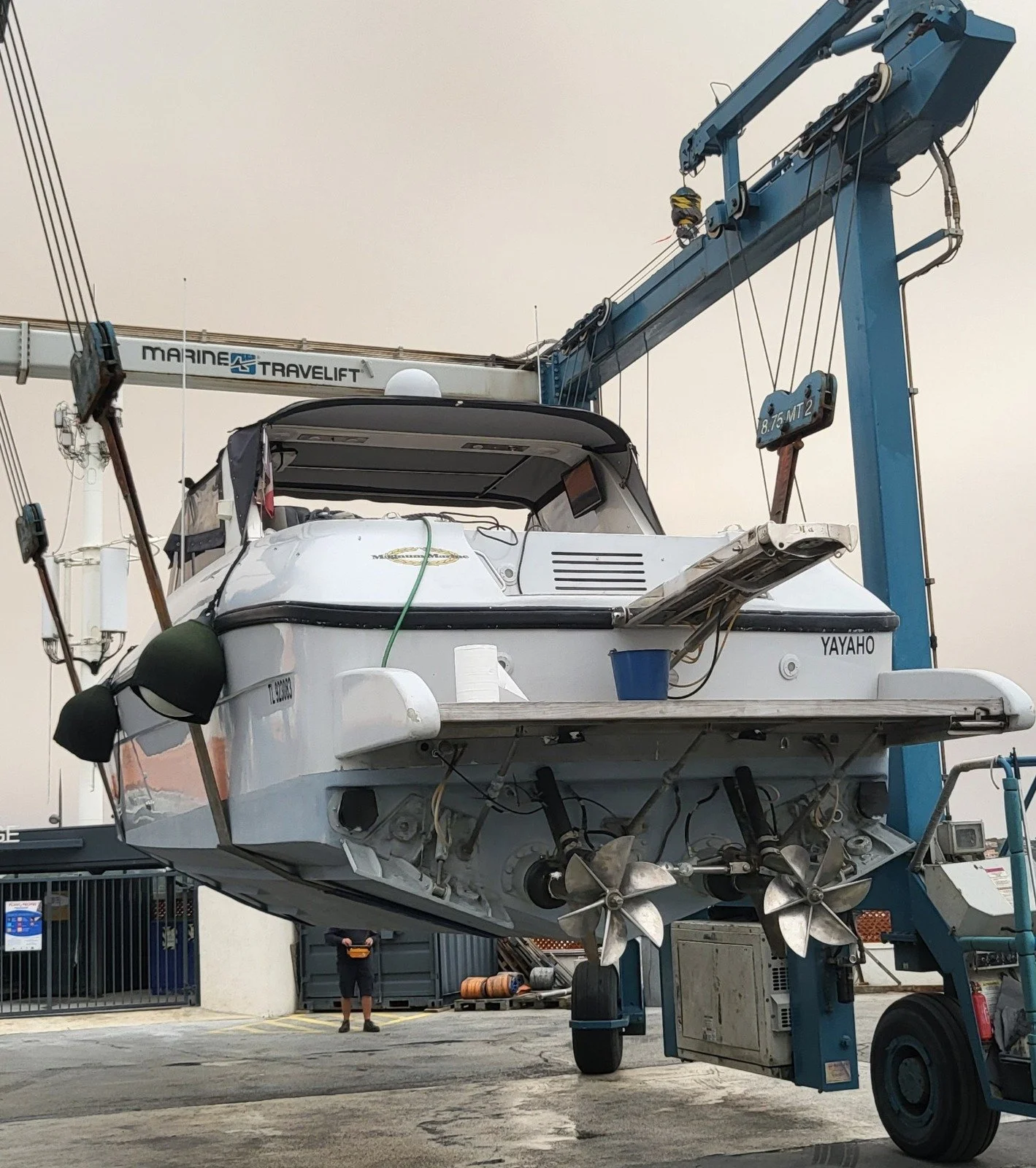 Un bateau enlevé par un grue à quai, vu de l'arrière avec deux hélices visibles, à l'aide d'une grue marine.