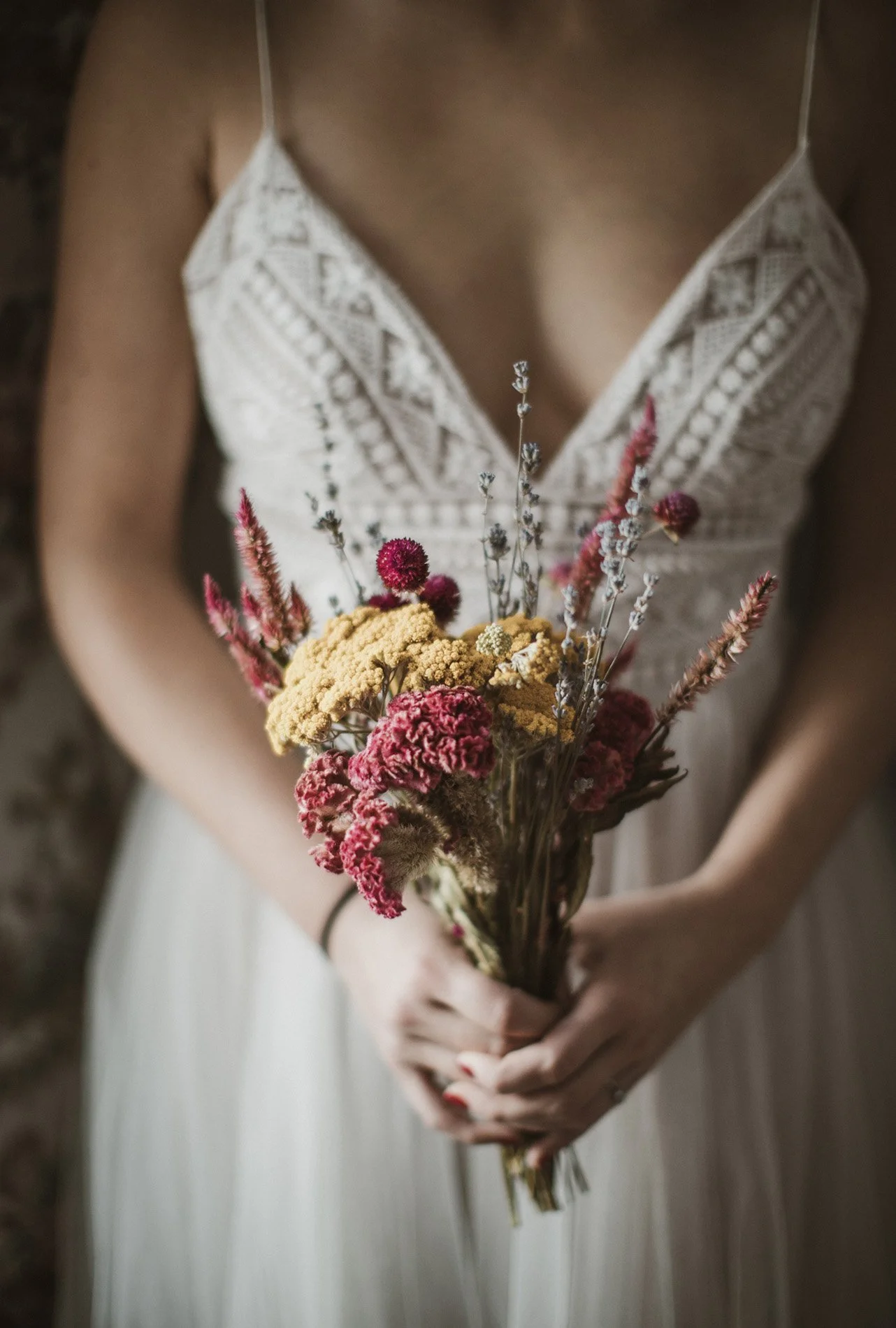 A woman in a white lace dress holding a bouquet of colorful dried flowers.