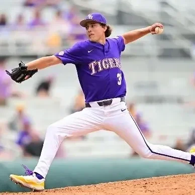 A baseball pitcher in a purple and white uniform mid-throw on the field.