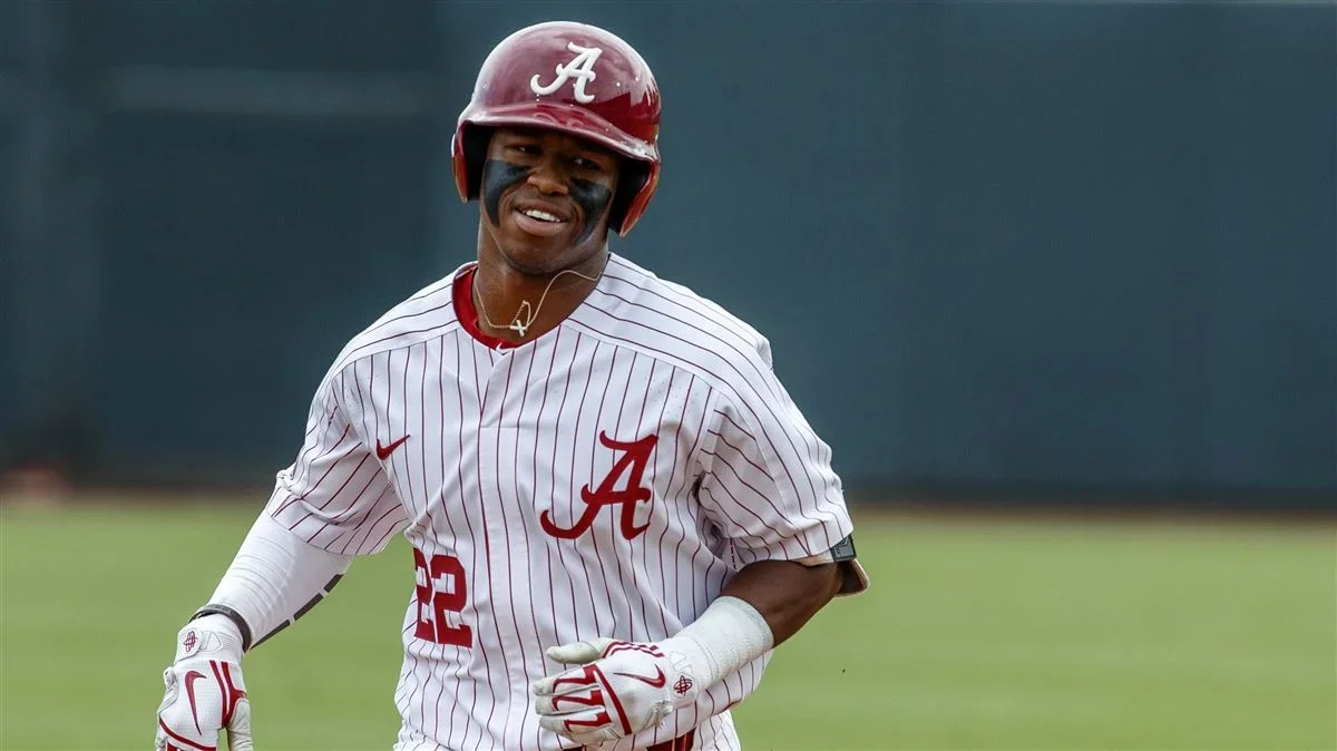 Baseball player wearing an Alabama jersey and helmet, smiling on the field