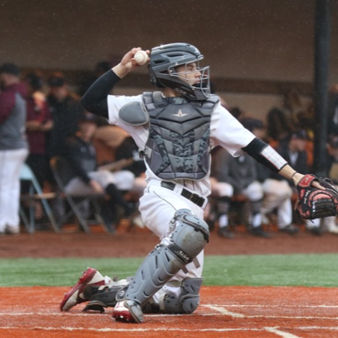 A baseball catcher batting during a game, wearing protective gear and a helmet, with fans in the background.