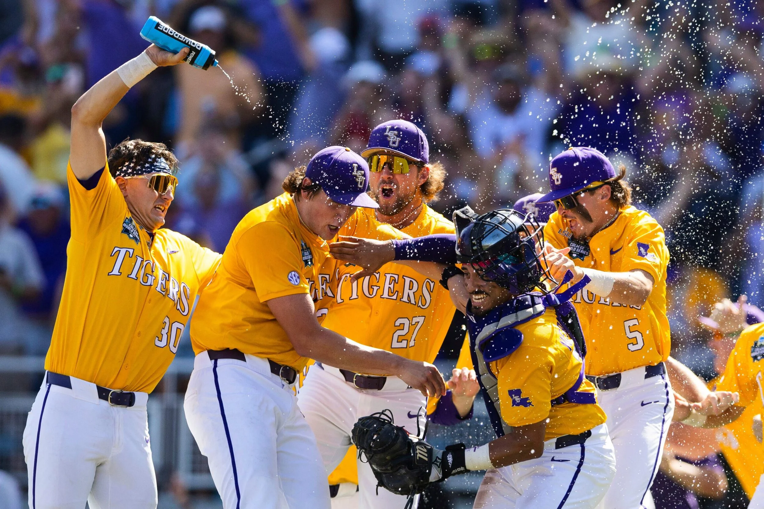 Baseball players from LSU Tigers celebrating, with water splashing around, during a game.