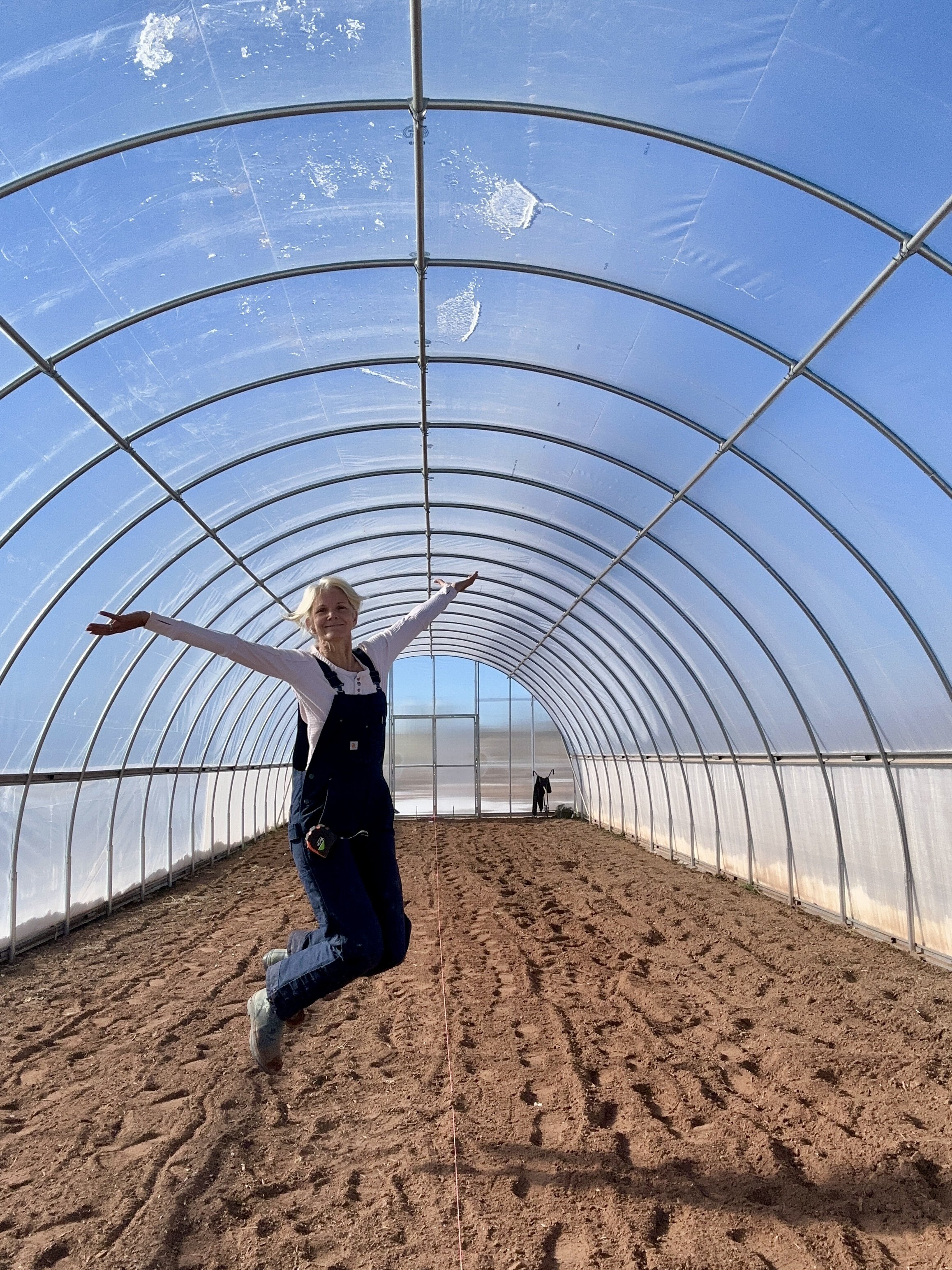 Woman wearing overalls, jumping for joy in a greenhouse.