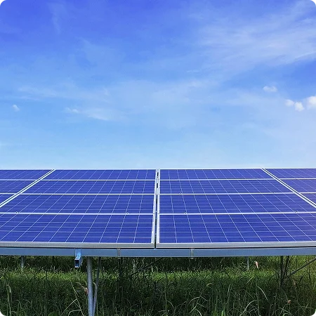 Solar panels installed on a grassy field under a blue sky with some clouds.