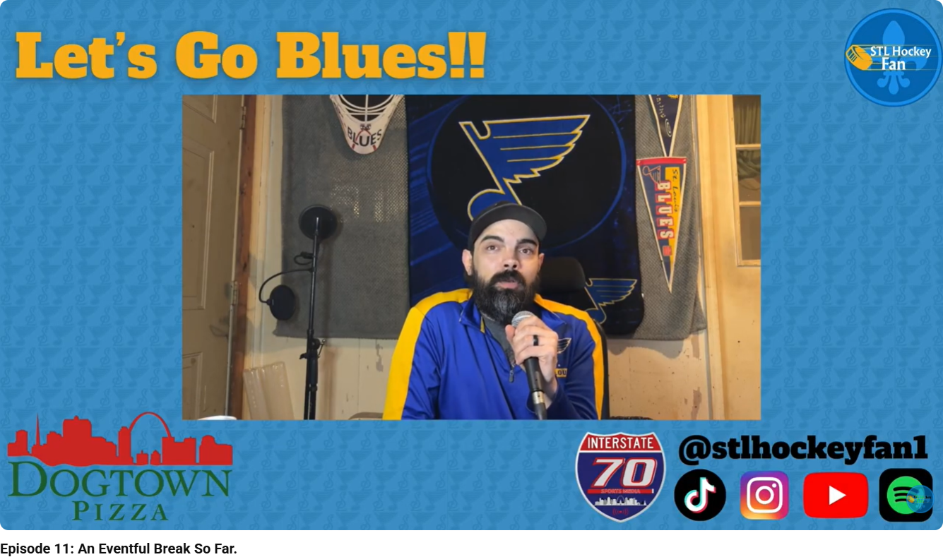 A man with a beard and dark hair, wearing a St. Louis Blues jacket, sitting at a table with a microphone, in a room decorated with St. Louis Blues hockey memorabilia, including a banner, pennant, and goalie mask. The graphic overlay says "Let's Go Bl