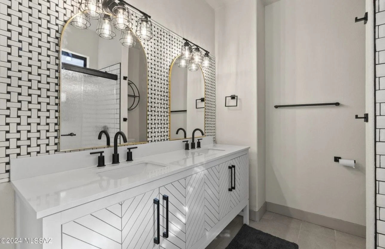Modern bathroom with twin mirrors, black fixtures, and a white vanity with a geometric design, black towel bars, and a textured wall behind the sink.