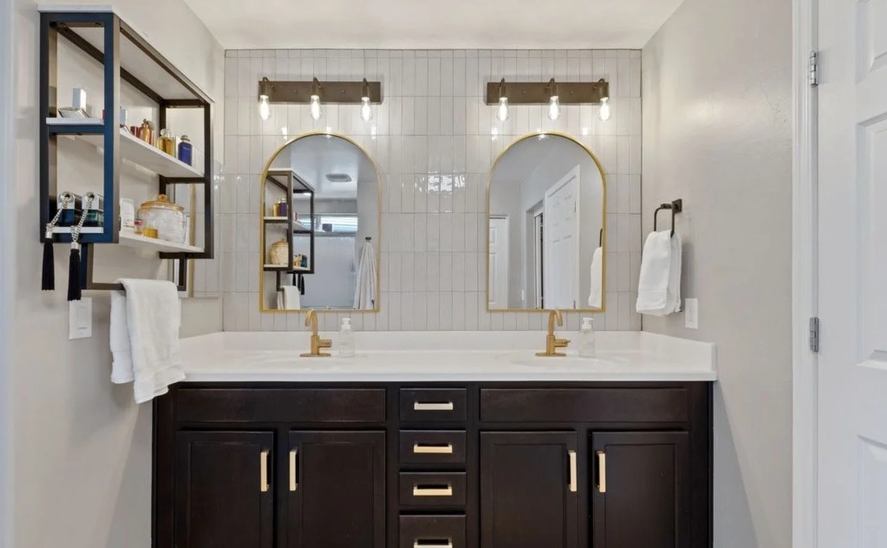 Double bathroom vanity with two mirrors, light fixtures, gold fixtures, dark cabinetry, and towels.
