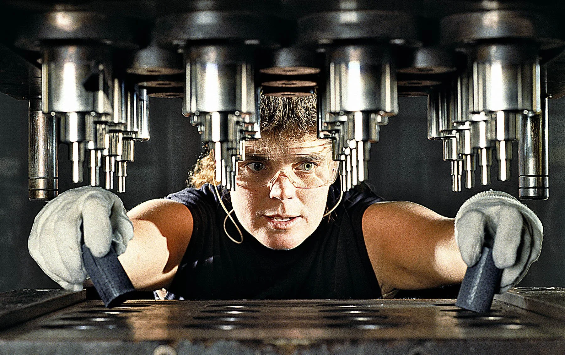 A machine operator loads plastic slugs into a molding machine producing automotive parts.