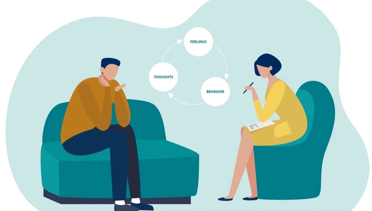 A man and a woman sitting across from each other in a therapy session. The woman is taking notes, and a flowchart showing the cycle between thoughts, feelings, and behavior is displayed above them.