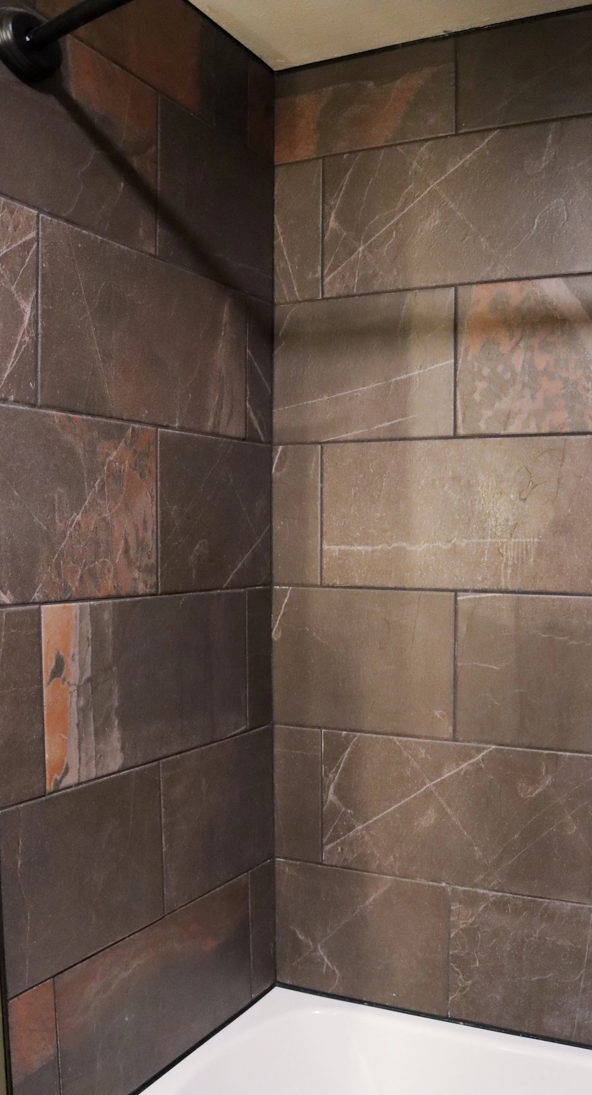 Close-up of a corner in a shower with brown marble tiles and a white shower base.
