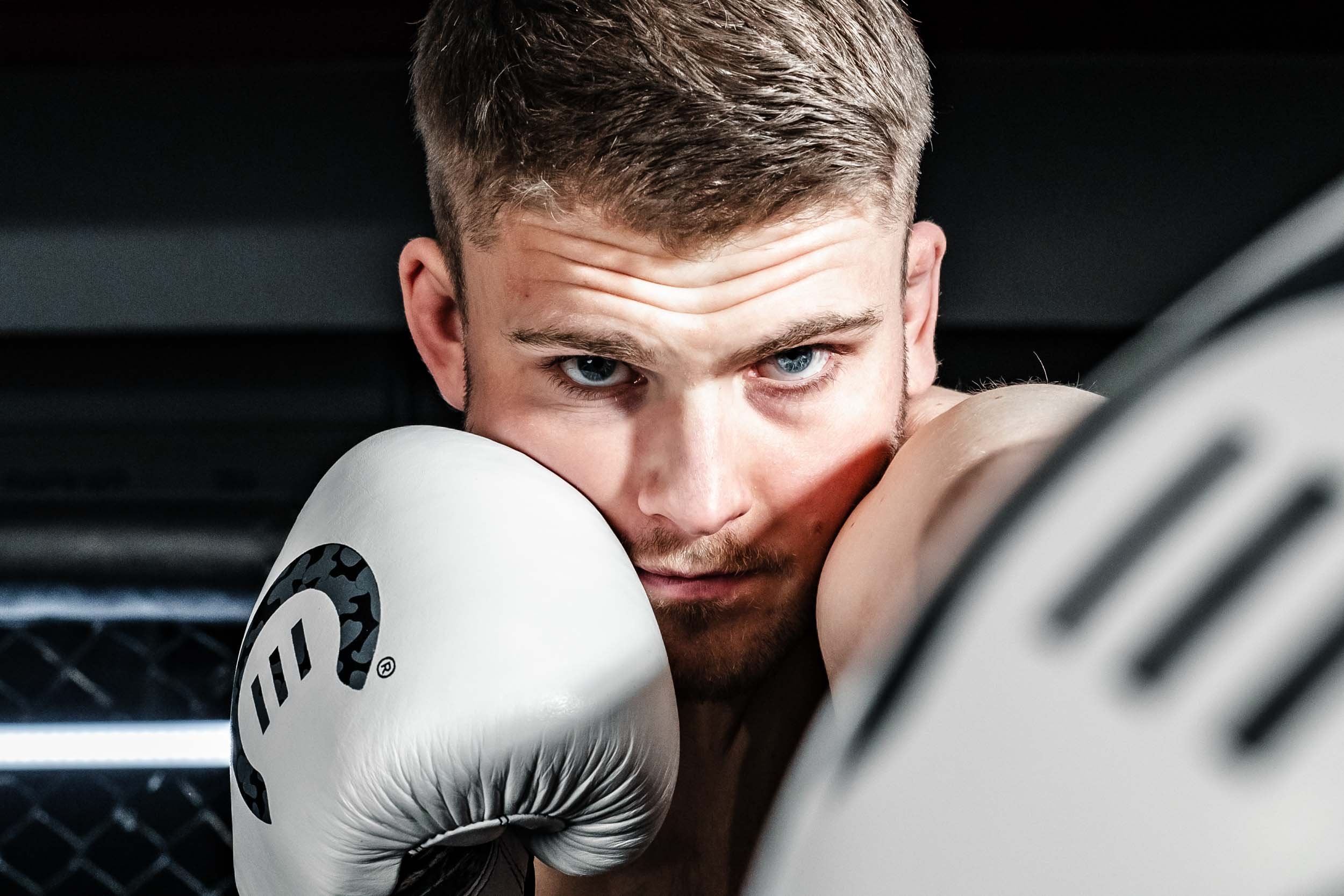 Nærbilde av en bokser med fokus på ansikt og hansker, med blå øyne og kort, lyst hår.