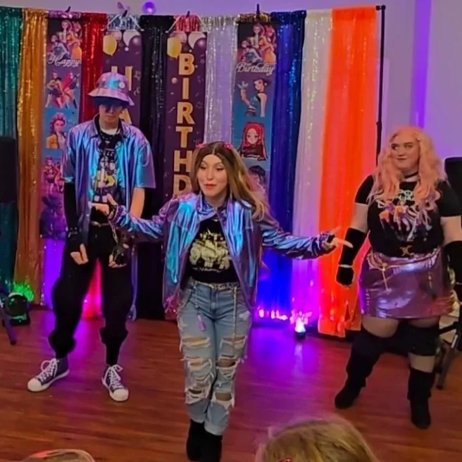 People celebrating a birthday with colorful themed decorations, including a backdrop with Streamer, banners, and a