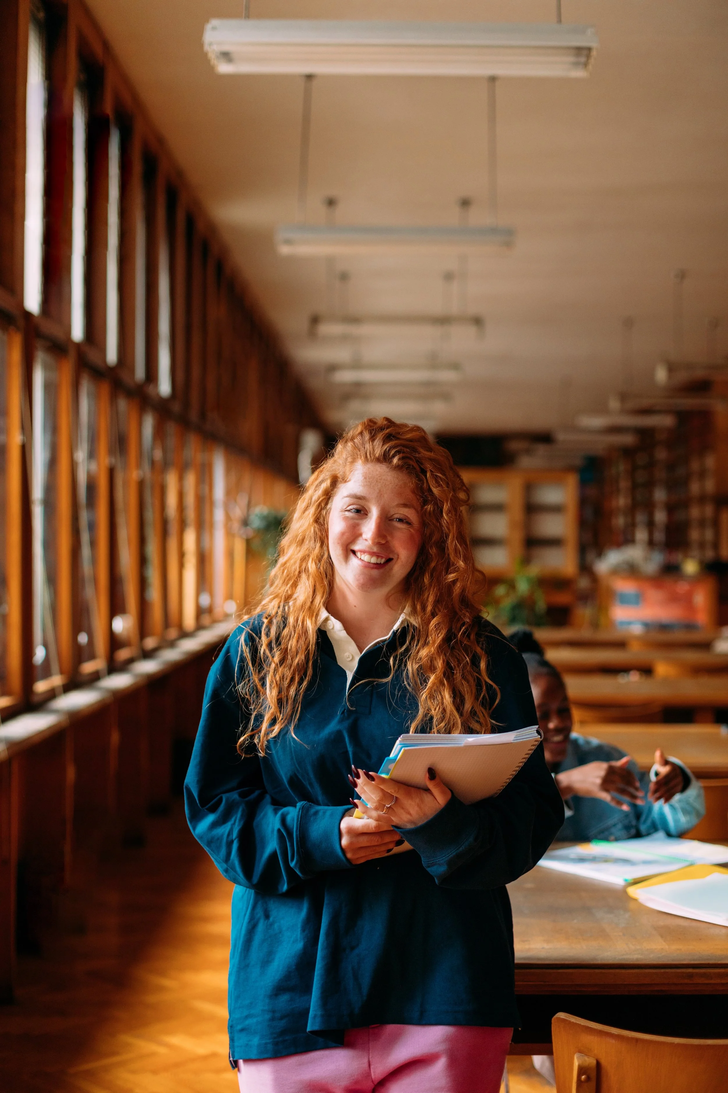 Smiling student holding notebooks in classroom setting.