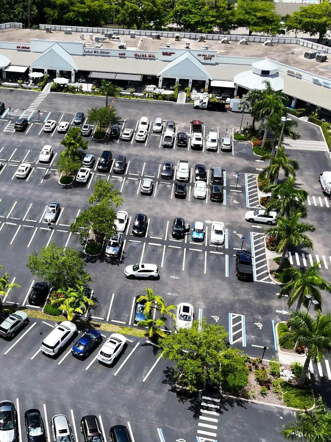 An aerial view of a shopping plaza parking lot with designated parking spaces, some marked for disabled parking, and improved traffic flow.