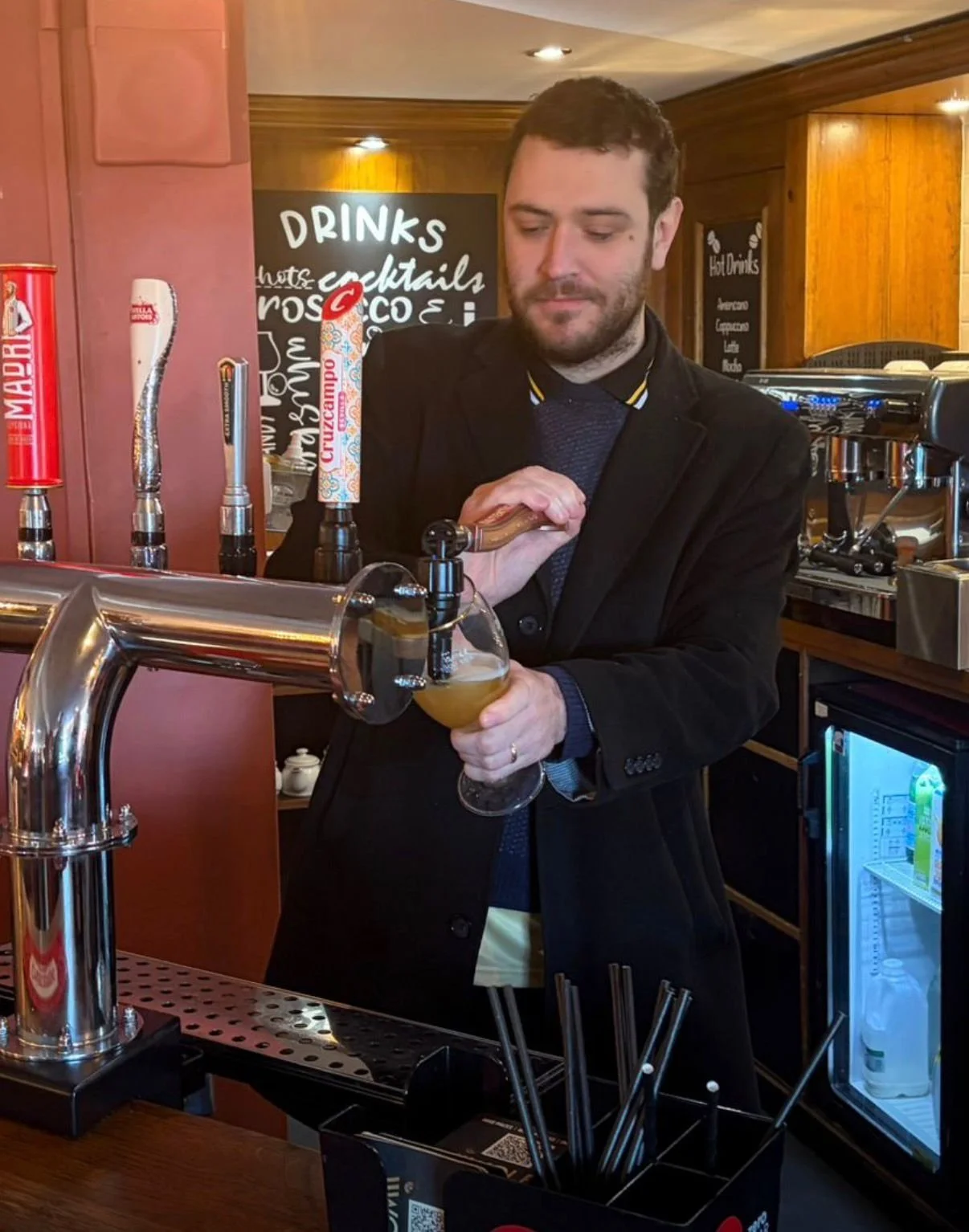 Man pouring beer from tap at bar, holding a glass.