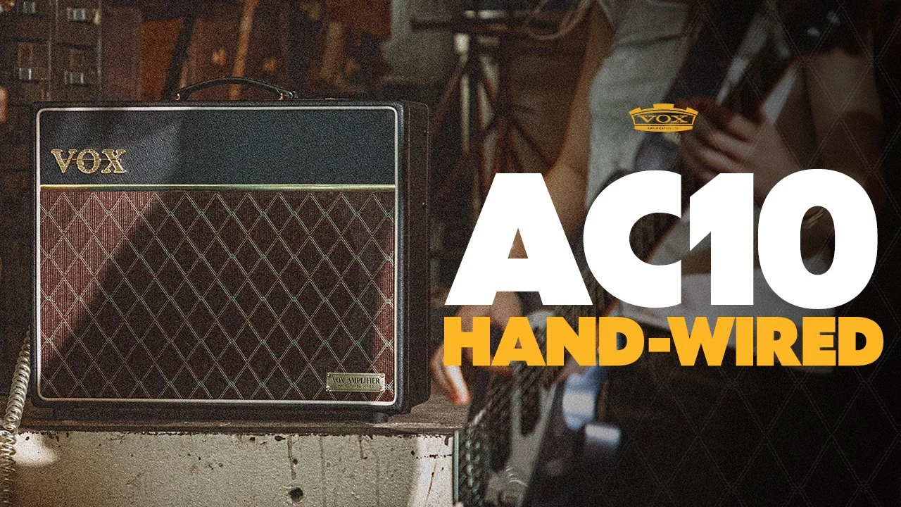 A VOX AC10 hand-wired guitar amplifier and a person holding an acoustic guitar in a room with a vintage and music studio setting.