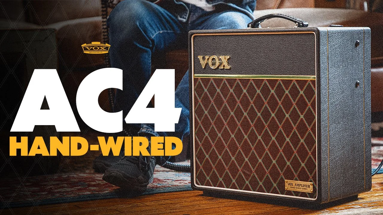 A VOX AC4 Hand-Wired guitar amplifier on a wooden floor, with a person sitting nearby wearing jeans and black shoes, as part of a music or recording setup.