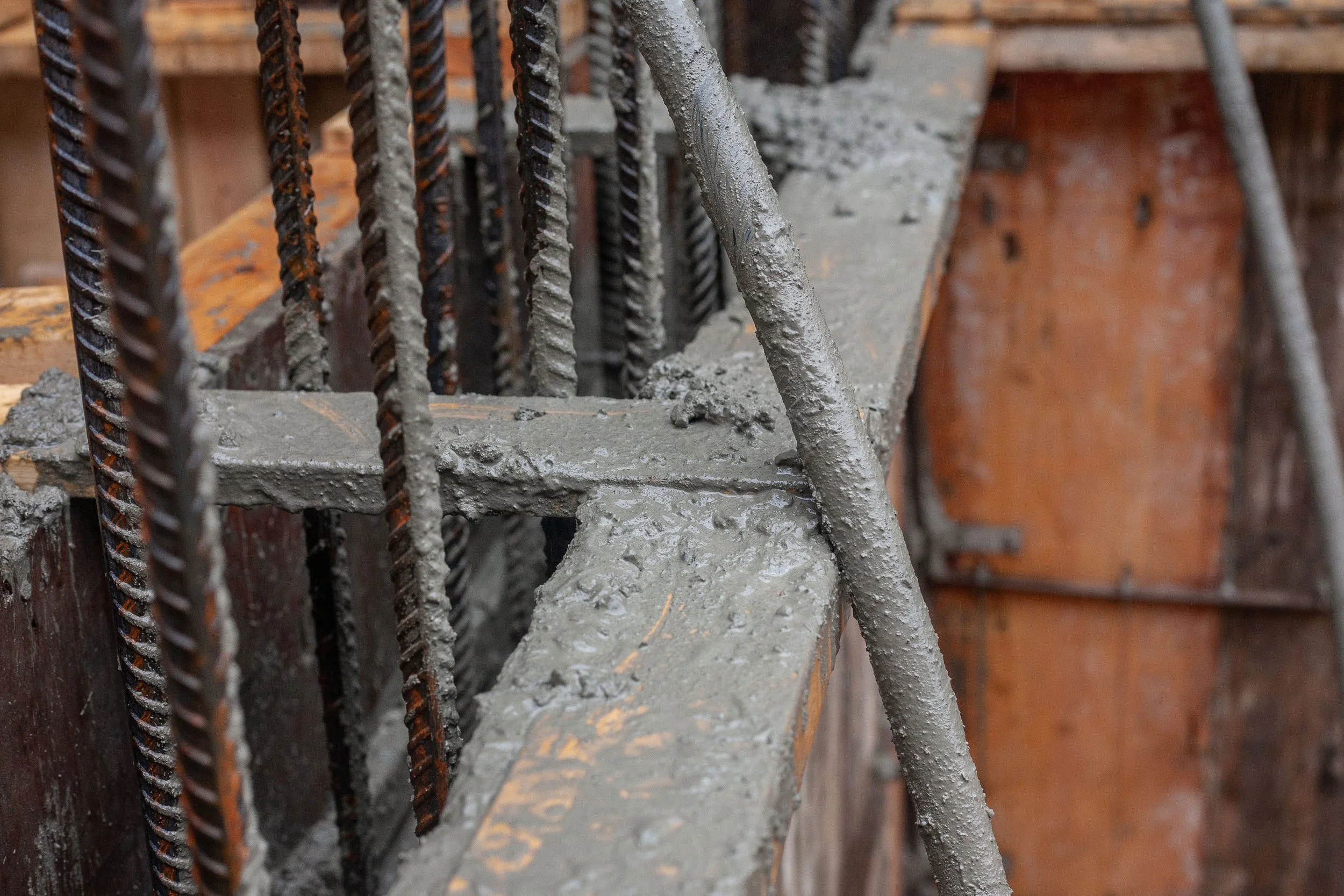 Close-up view of steel rebar and concrete on a construction site with wooden formwork in the background.