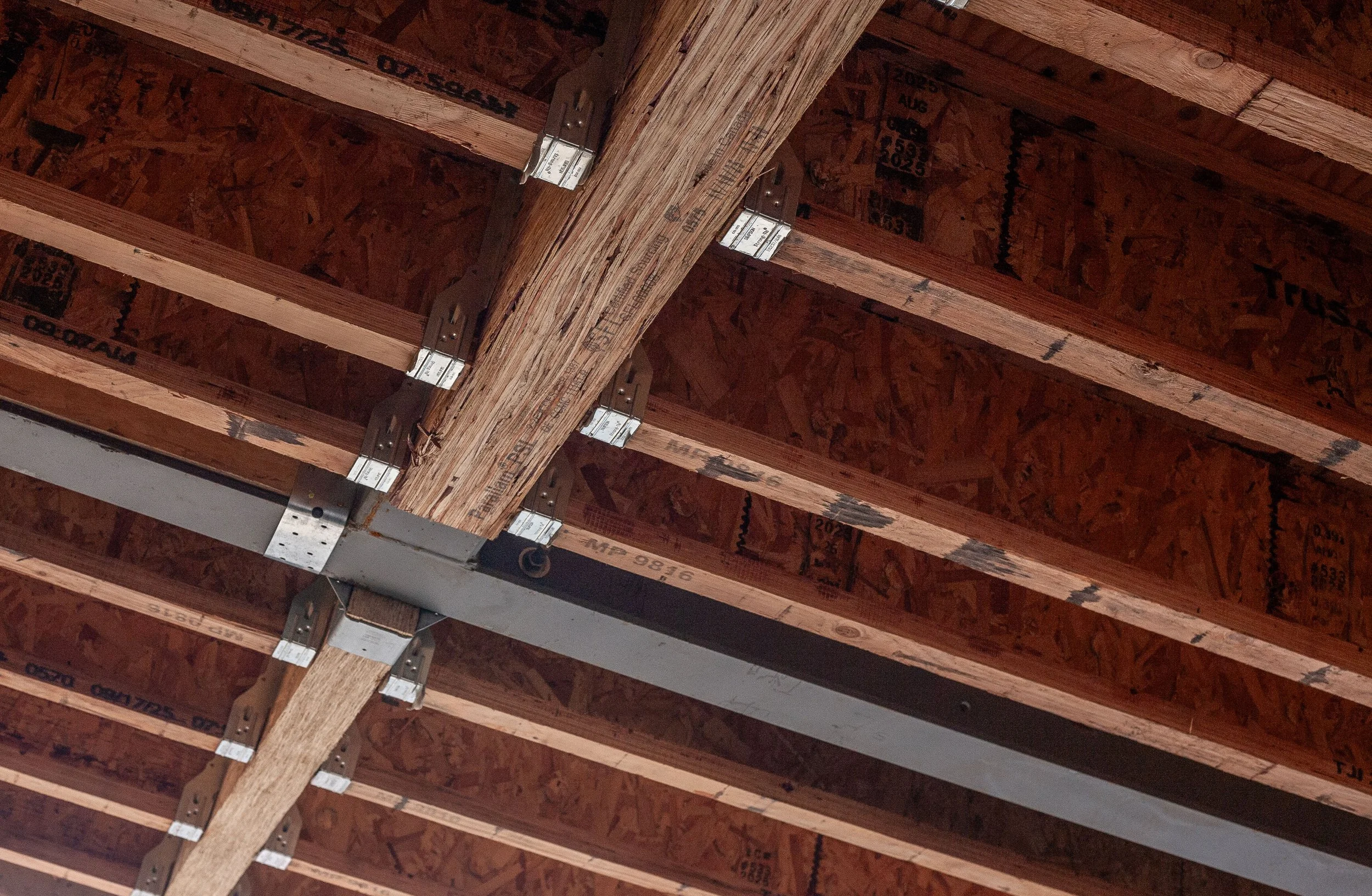 Close-up view of a ceiling structure under construction, showing wooden beams, metal brackets, and a metal support beam.