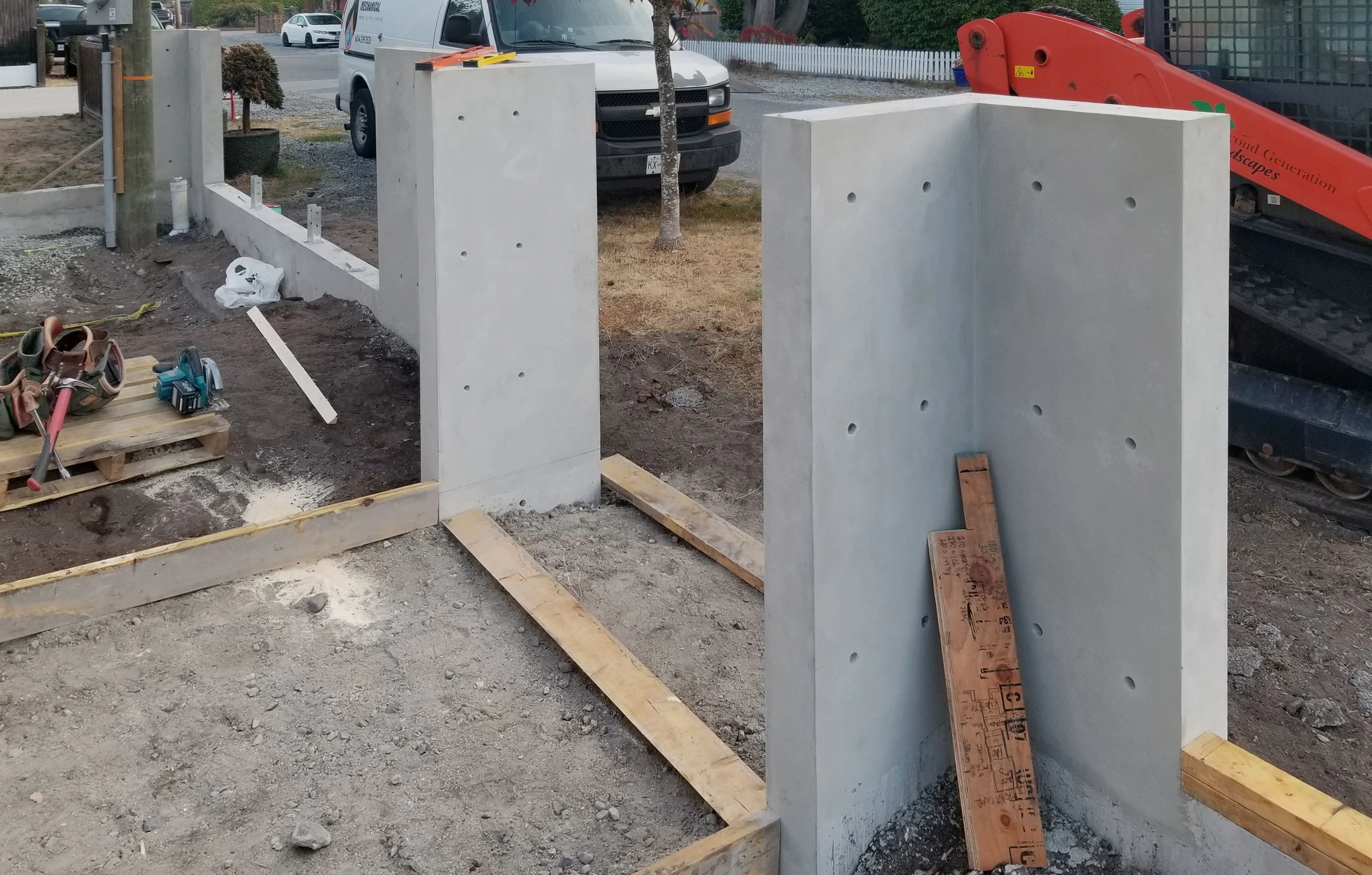 Construction site with concrete pillars being installed, wooden supports, tools, and construction equipment present.