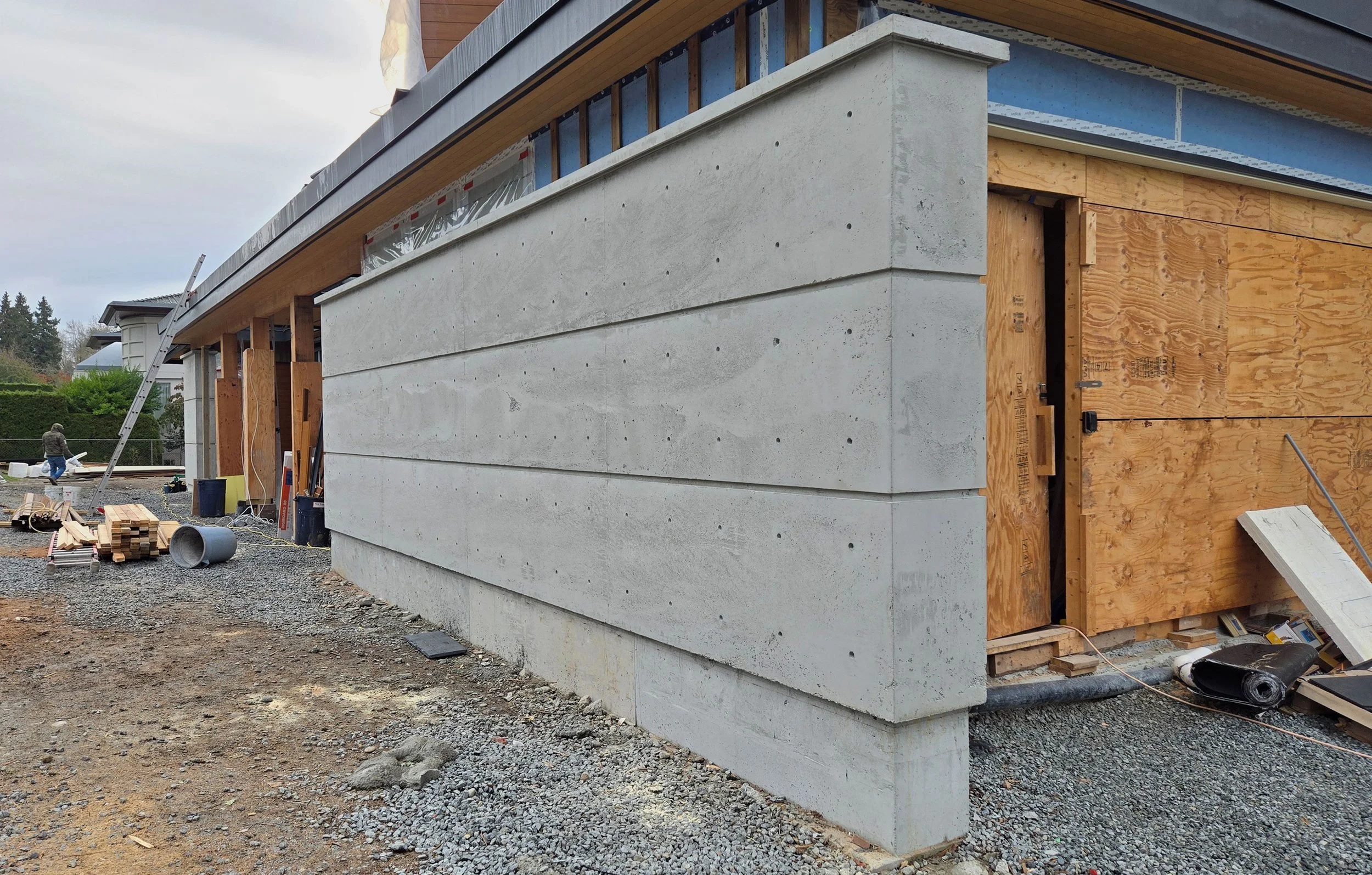 Building under construction with concrete and wood walls, construction equipment, and workers on-site.
