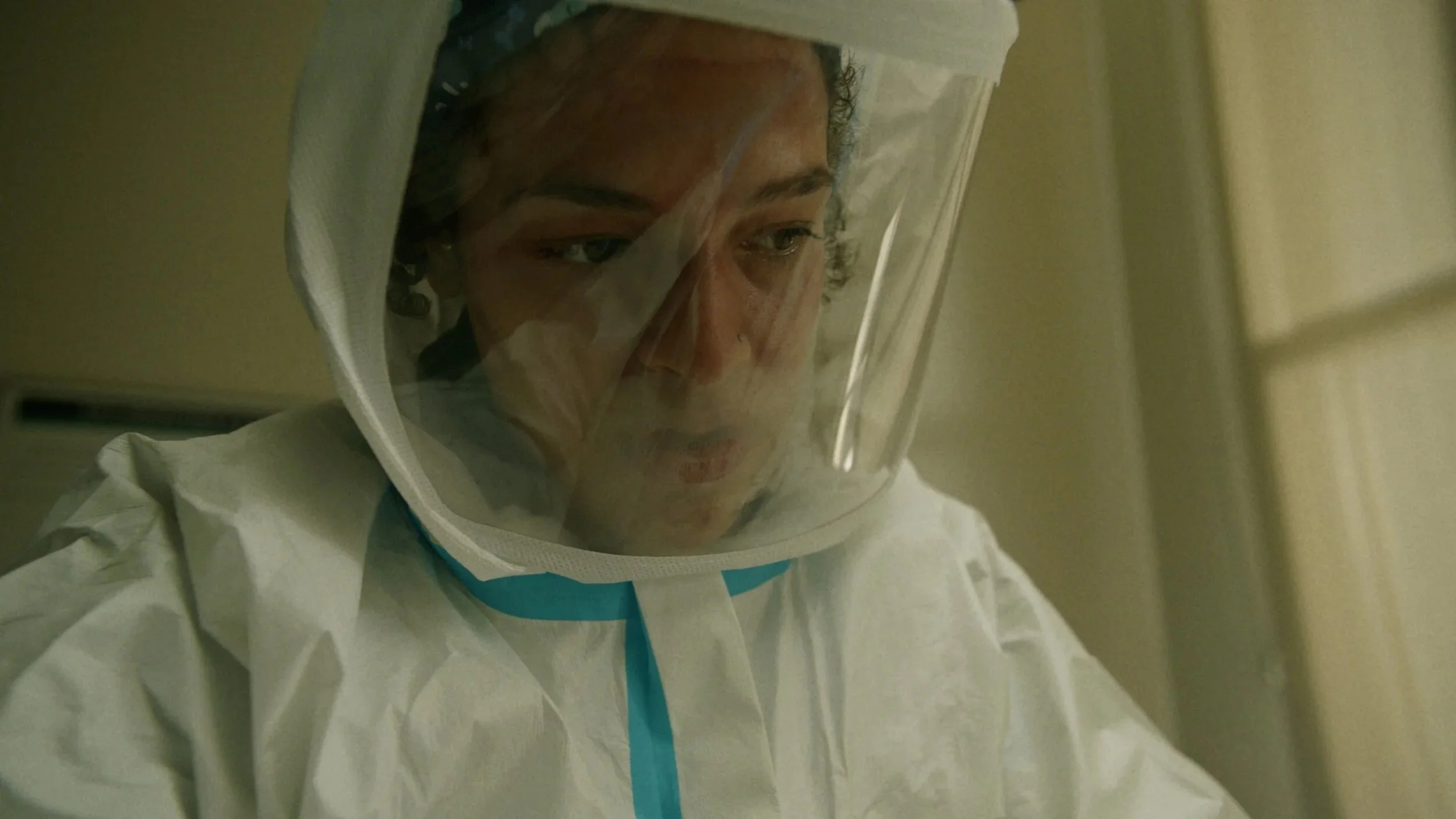 A healthcare worker in personal protective equipment, including a white suit and face shield, working in a clinical setting.