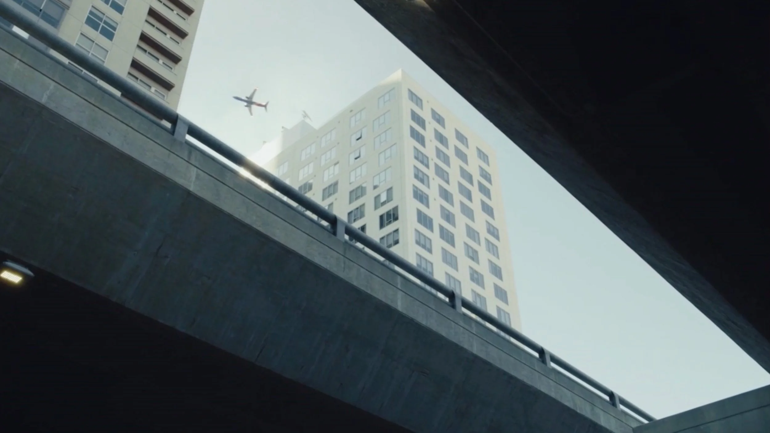 Looking up at a tall white building through a concrete overpass with two airplanes flying in the sky above.