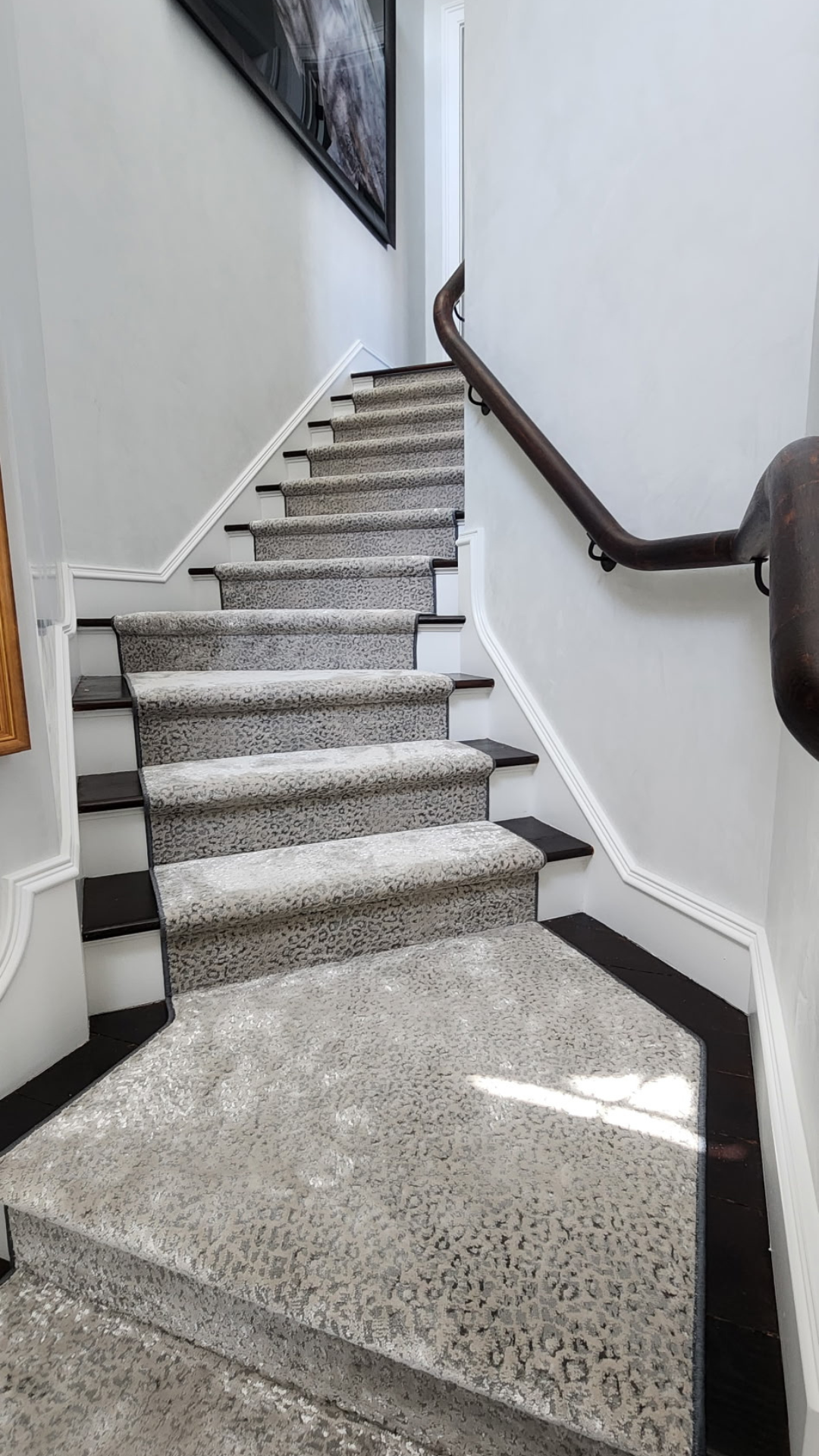 Carpeted staircase with a curved dark wooden handrail on the right and a white wall on the left, leading upward to a door at the top.