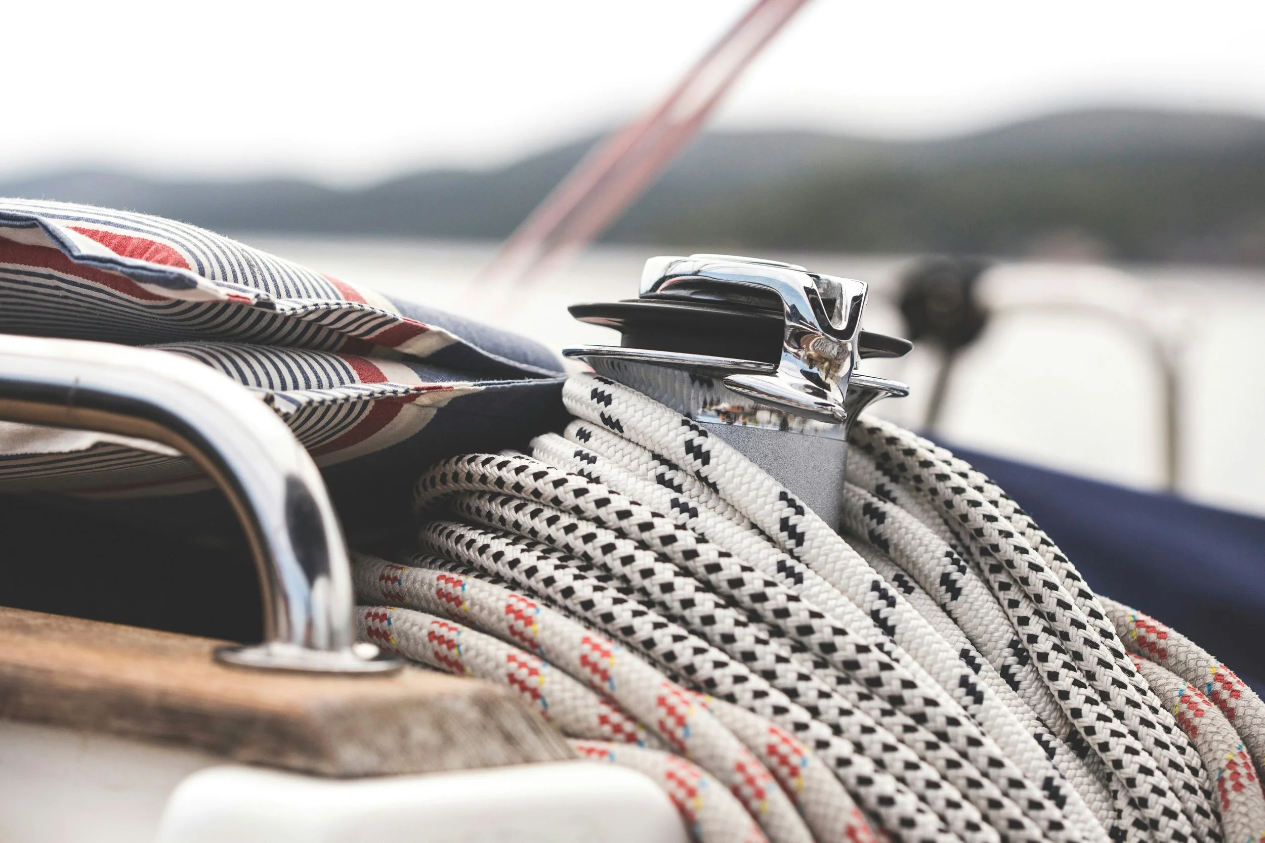Close-up of a sailing rope and winch on a boat with a fabric cushion nearby.