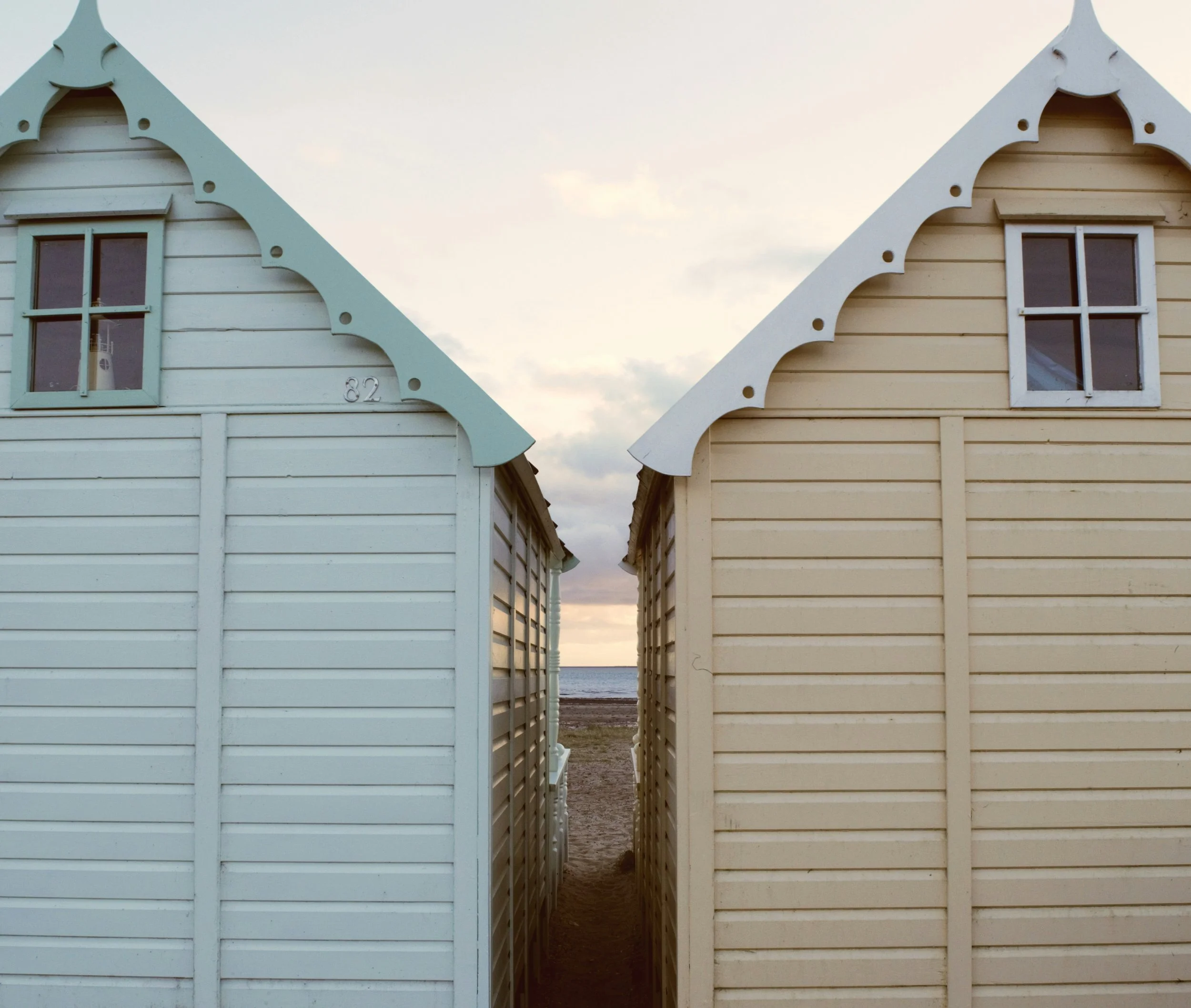 Colorful beach houses with decorative trim facing the ocean, between two structures.