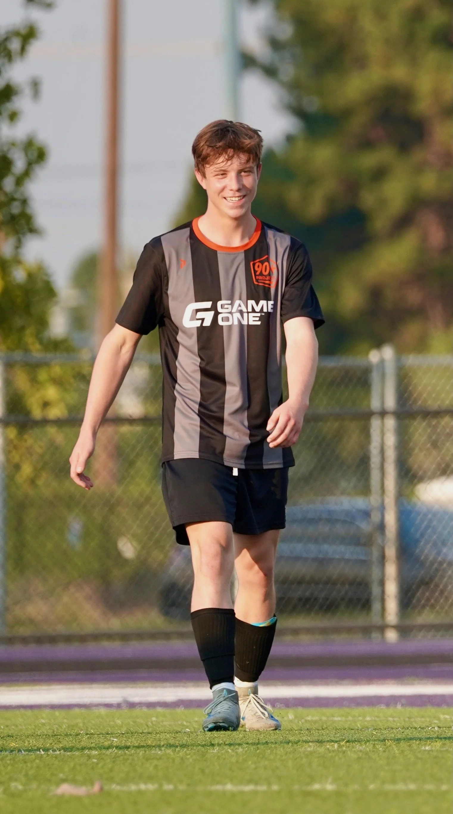 Young man in a black and gray soccer uniform with the words 'GAME ONE' on the front, standing on a soccer field.