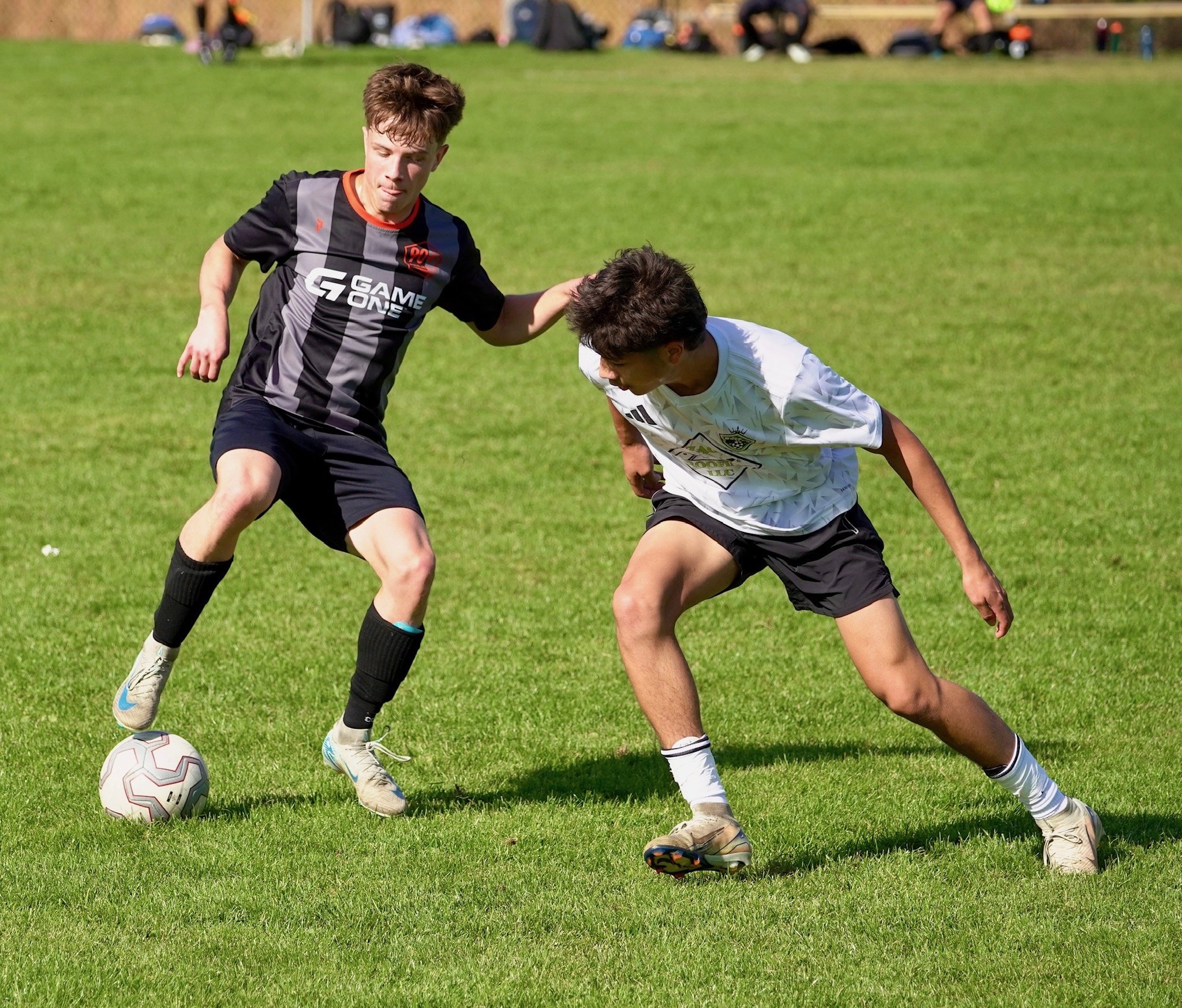 Two boys playing soccer on a green field, one in a black jersey and the other in a white jersey, competing for the ball.