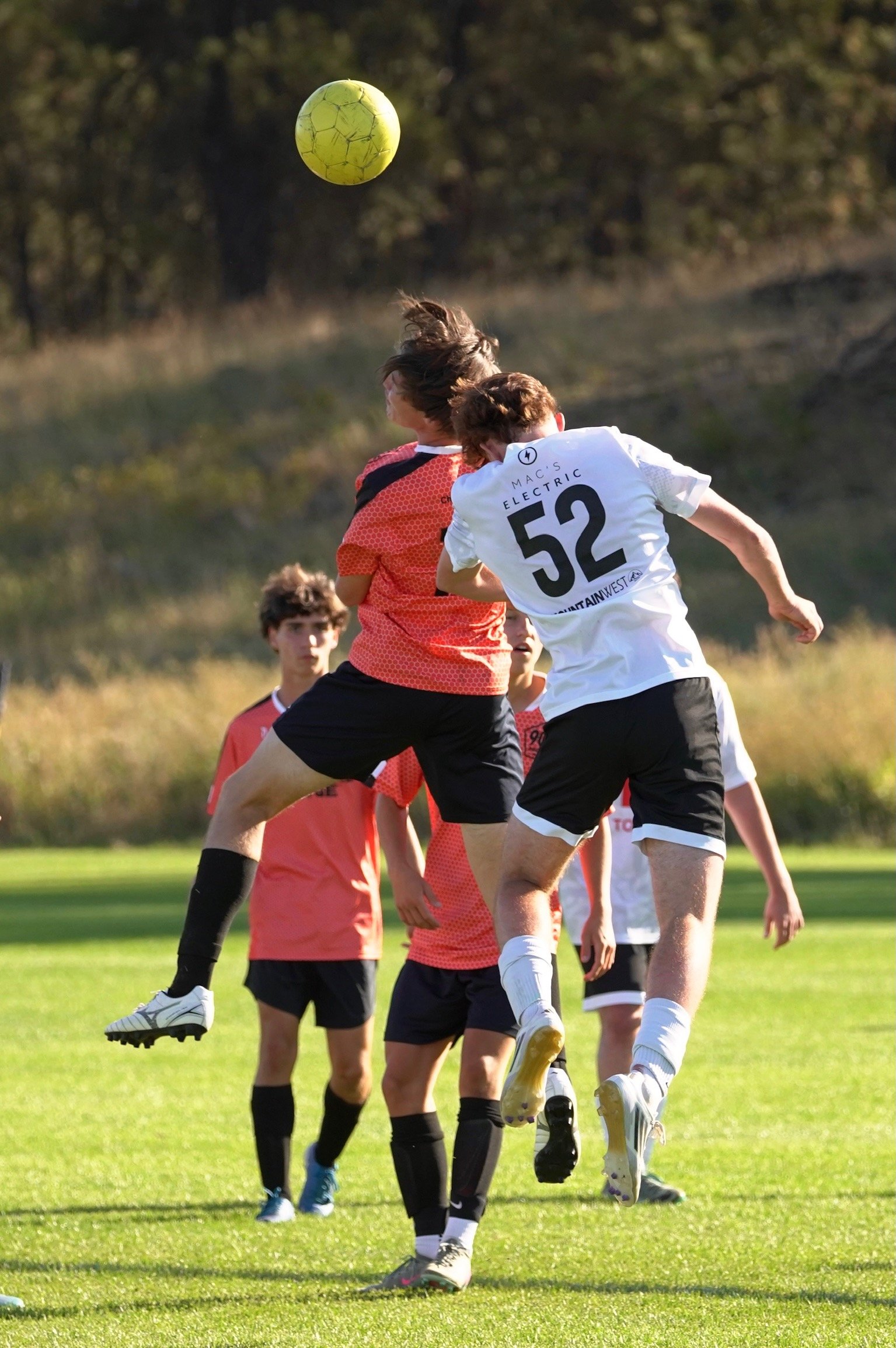 Soccer players jumping to head the ball on a grassy field during a game.