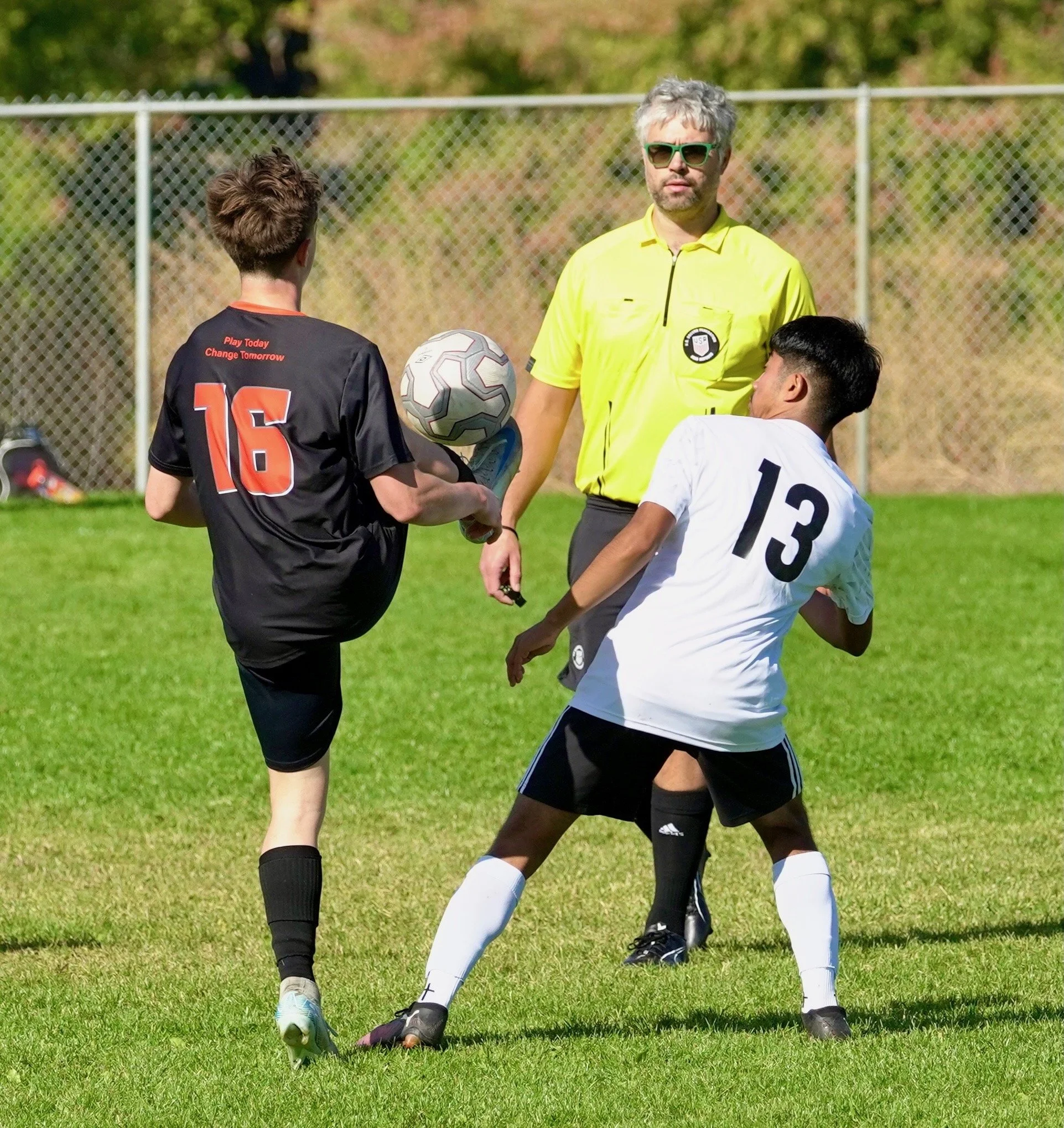 Two soccer players competing for the ball during a game, with an official overseeing the play on a grassy field.