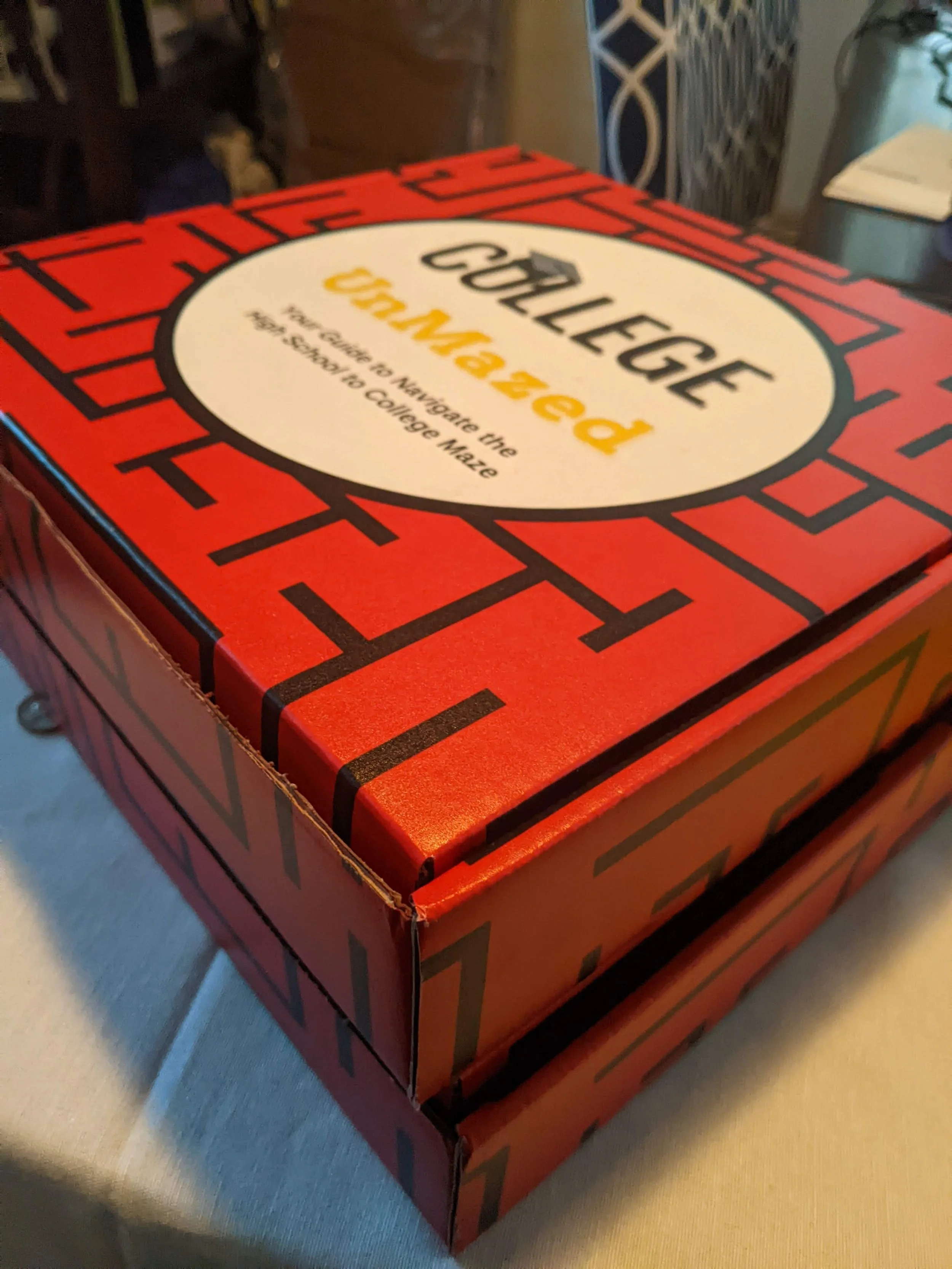 Stacked red boxes with black maze design and 'College UnMazed' text on top box.