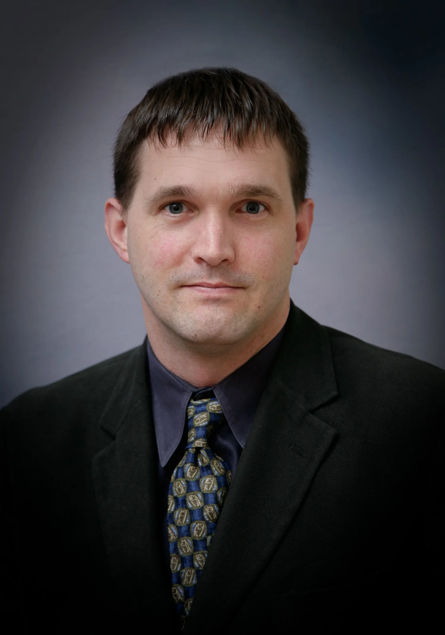 Man in a suit and tie posing for a portrait against a neutral background.