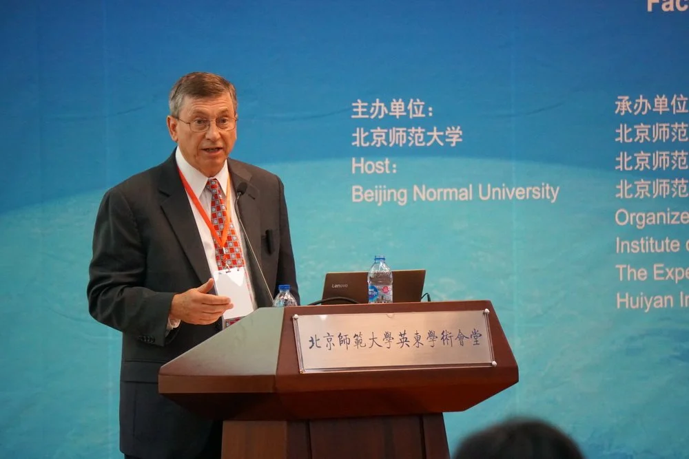 A man giving a presentation at Beijing Normal University, speaking at a podium with a microphone. The background features text in both Chinese and English, indicating the event is hosted by Beijing Normal University.