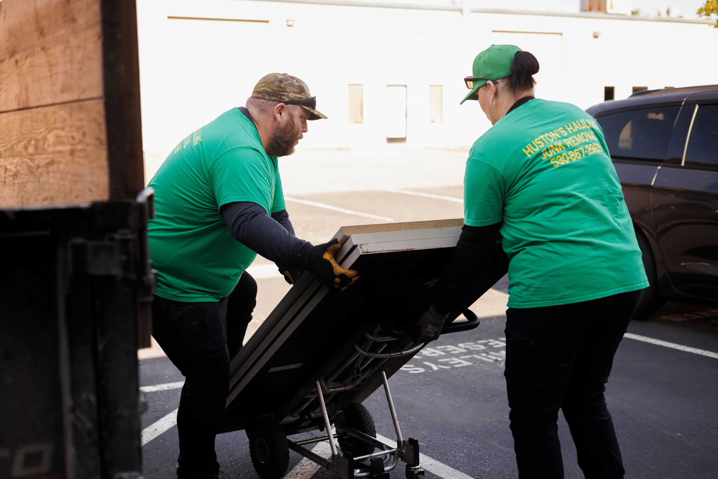 Ross and Melissa Huston of Huston’s Hauling Junk Removal moving dismantled cubicle desk tops on a dolly beside a hauling trailer during cleanup of the future EnKore Theatre Company space.